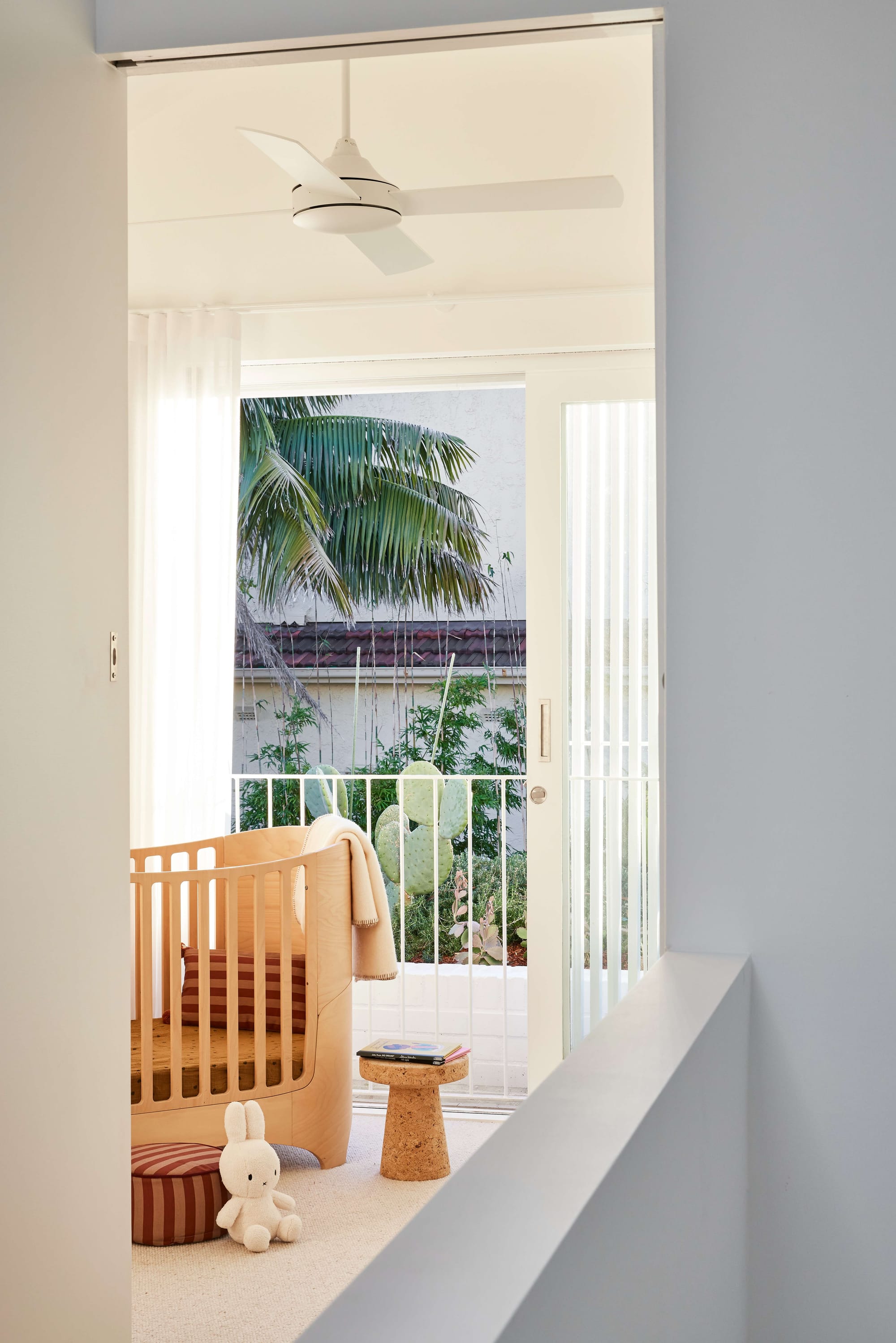 North Bondi House by Studio Arkive. Photography by Pablo Veiga. Nursery with timber crib, cord stool, light carpets, and balcony with white fencing. 