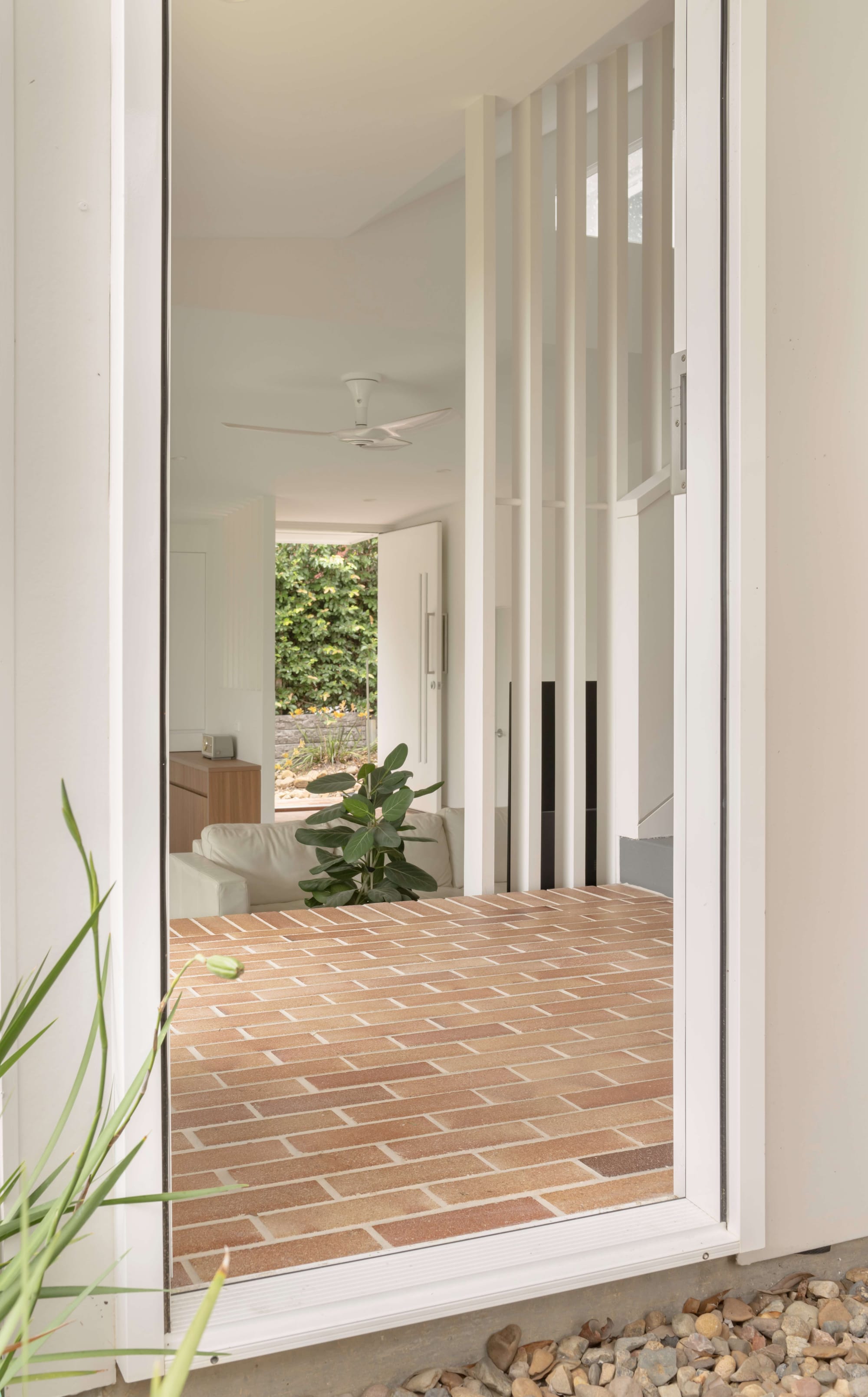 Oates by LOUPE Architecture. Photography by Alanna Jayne McTiernan. Brick flooring framed through a white window frame, with a living area beyond. 