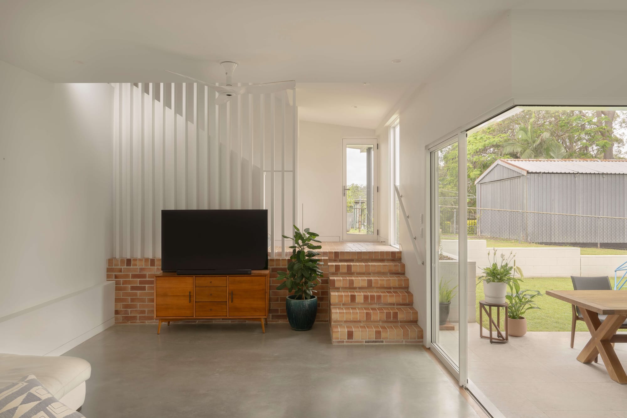 Oates by LOUPE Architecture. Photography by Alanna Jayne McTiernan. Multilevel living space with brick stairs, polished concrete flooring, and full height sliding doors opening onto a paved outdoor dining area. 