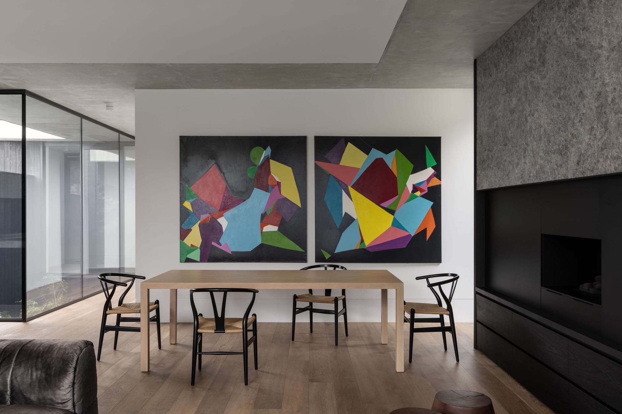 Osbourne by Mancini Made. Photography by Timothy Kaye. Dining space wih stone textured walls, abstract art, timber furnishings and flooring, and crisp white walls and black framed windows.