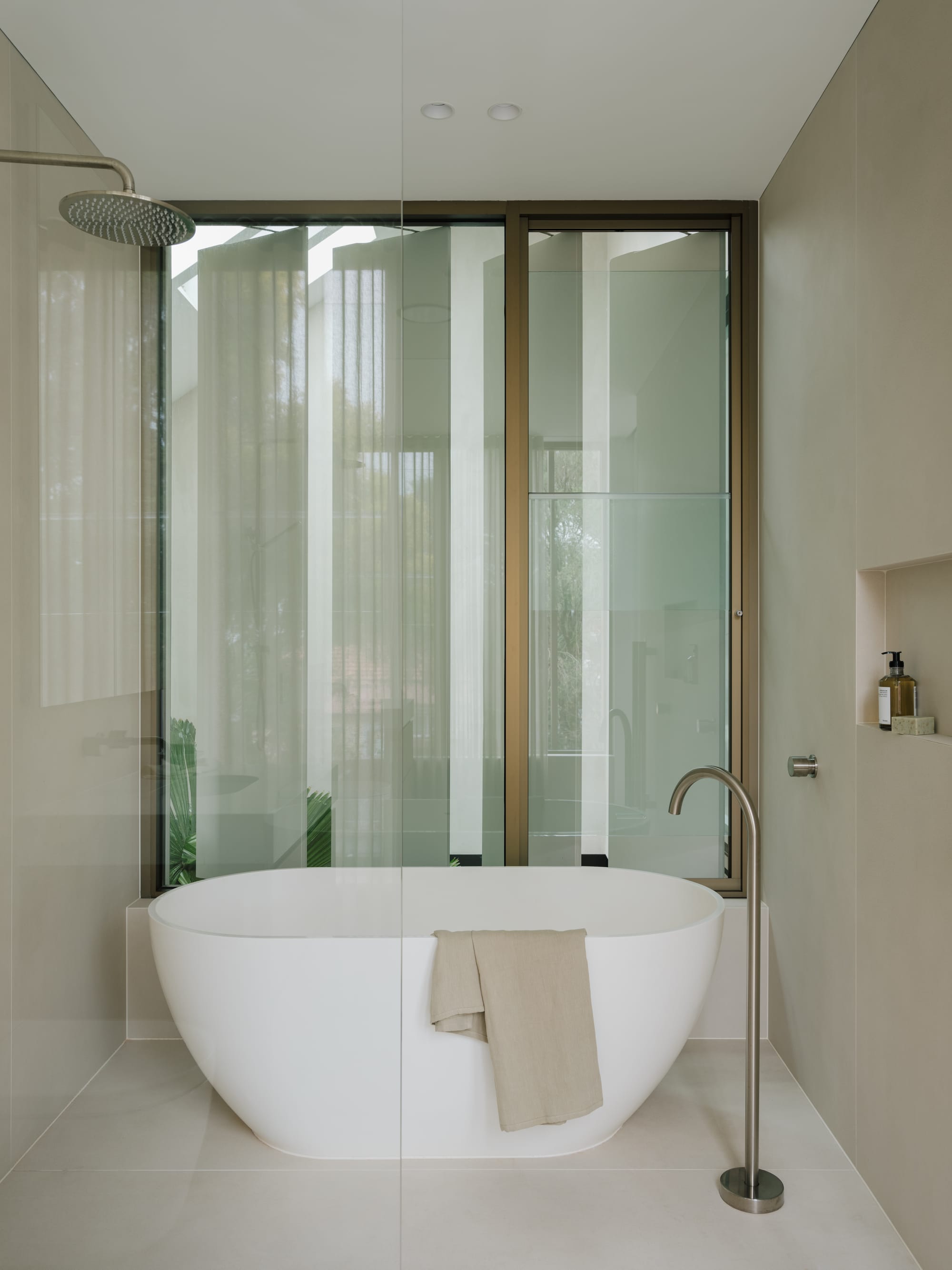 Petersham House by Cateaux Architects with CHROFI. Photography by Clinton Weaver. Free standing white bathtub in front of glass window in bathroom with beige floor and wall tiles. 