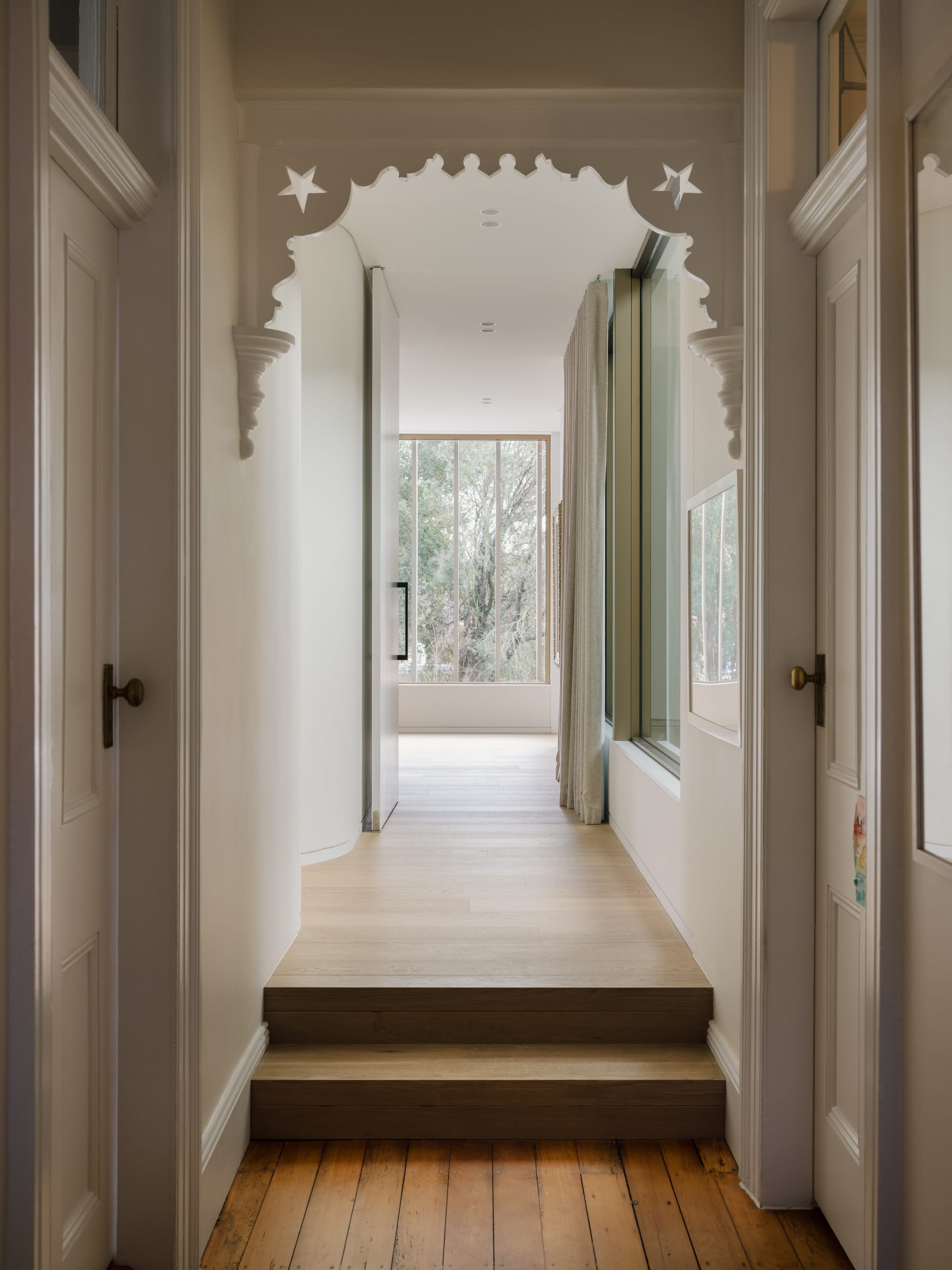 Petersham House by Cateaux Architects with CHROFI. Photography by Clinton Weaver. Hallway with new and old timber flooring separated by a step and an ornate heritage door arch.