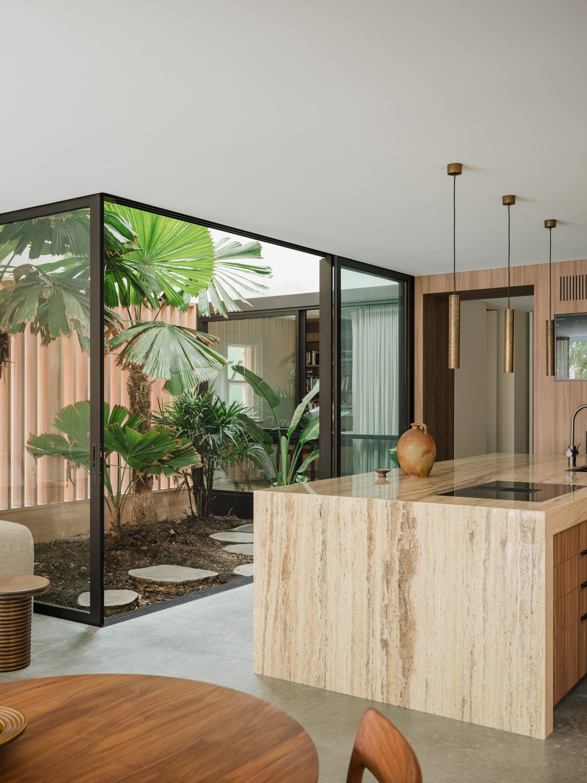 Petersham House by Cateaux Architects with CHROFI. Photography by Clinton Weaver. Kitchen with polished concrete flooring, stone island bench, and black framed floor length sliding doors leading to a lush courtyard. 