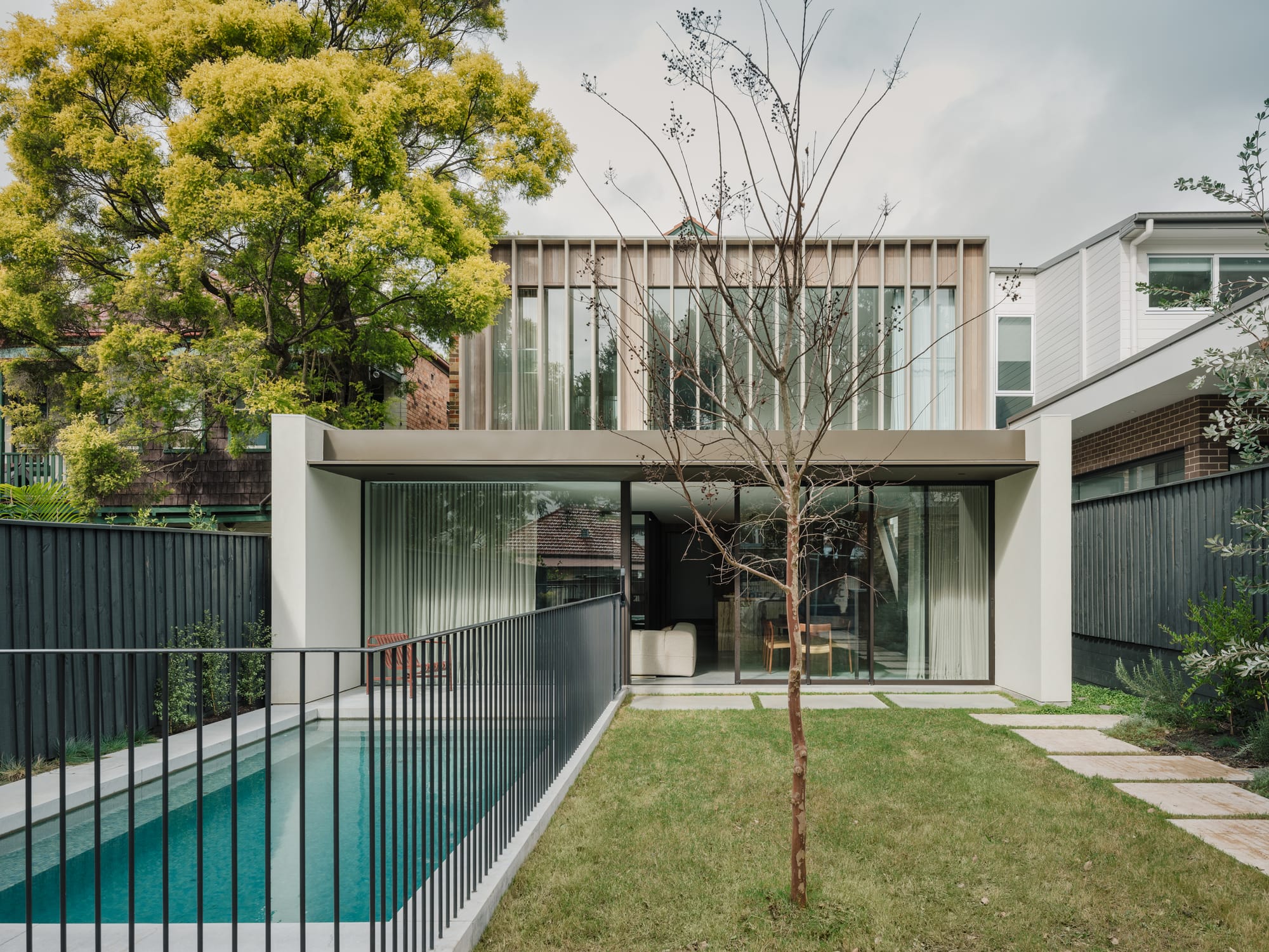 Petersham House by Cateaux Architects with CHROFI. Photography by Clinton Weaver. Rear facade of two-storey contemporary home with a pool to the left, gras to the right and white external paint. 