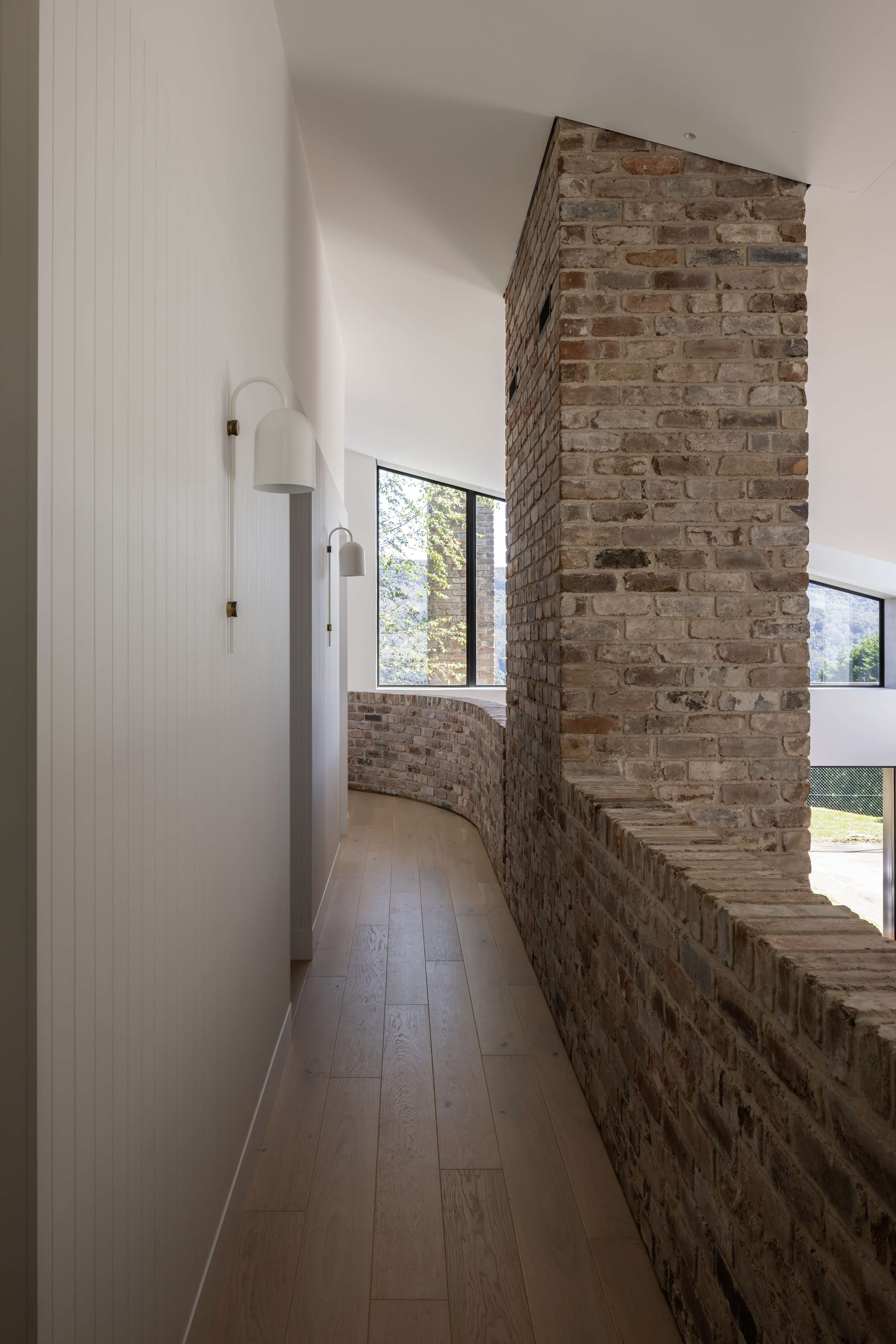 Wicklow Hills by Robertson Collectif. Photography by Simon Whitbread.  Hallway with whit timber clad wall to the left and reclaimed brick curved half wall to the right. Timber flooring throughout. 