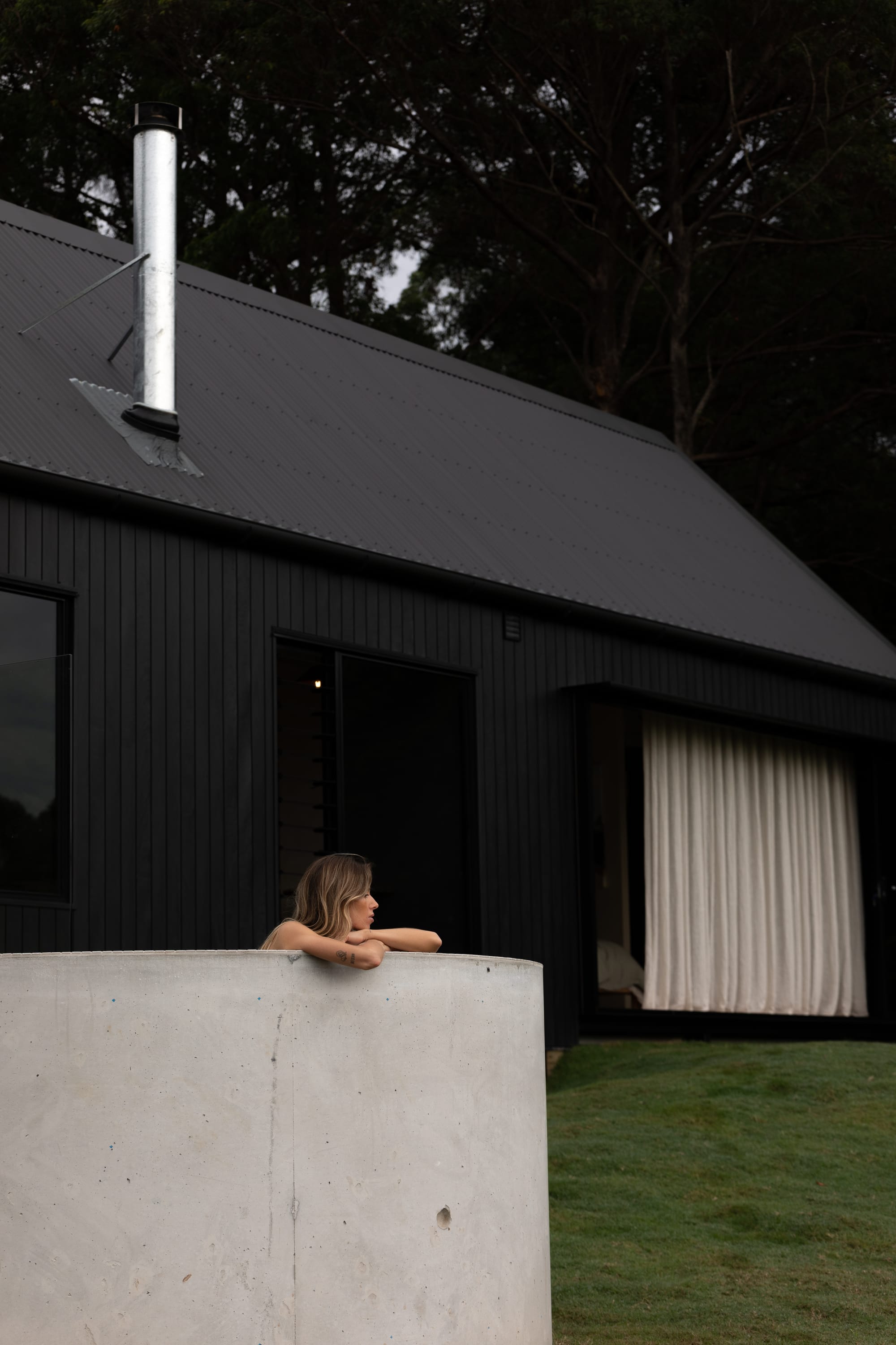 Round Hill Retreat by Round Hill Projects x SI.DE Architecture. Photography by Tim Birch. Woman in round tiled outdoor pool overlooking dense treetop landscape.