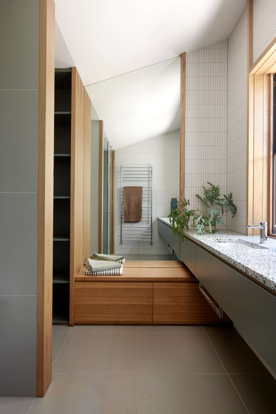 Eaglemont House by BENT Architecture. Photography by Tatjana Plitt. Bathroom with grey floor tiles, green and terrazzo counter, timber bench and full height mirror.