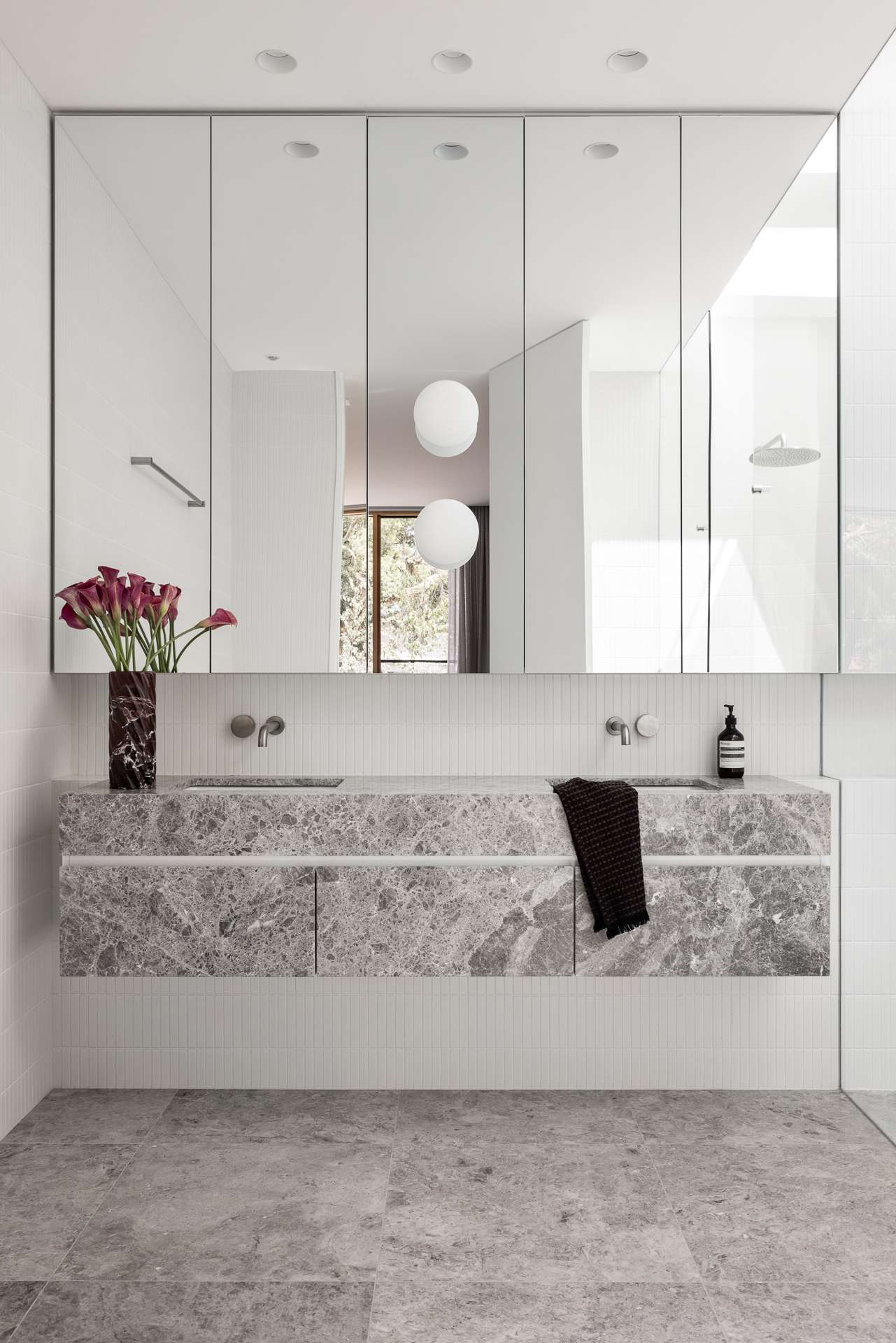 Bastings House by FURNISHD. Photography by Dylan James.  Bathroom with marbled grey floating vanity, grey tiled floors, white finger tiled walls and a large vanity mirror. 