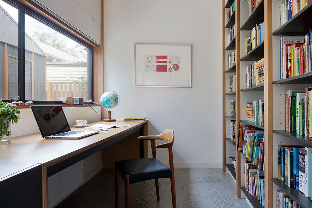 Thornbury House by BENT Architecture. Photography by Tatjana Plitt. Office space in residential home with floor to ceiling bookshelves on righthand hall, timber desk below a window on left hand wall, and wall art and collected decor on white walls. 
