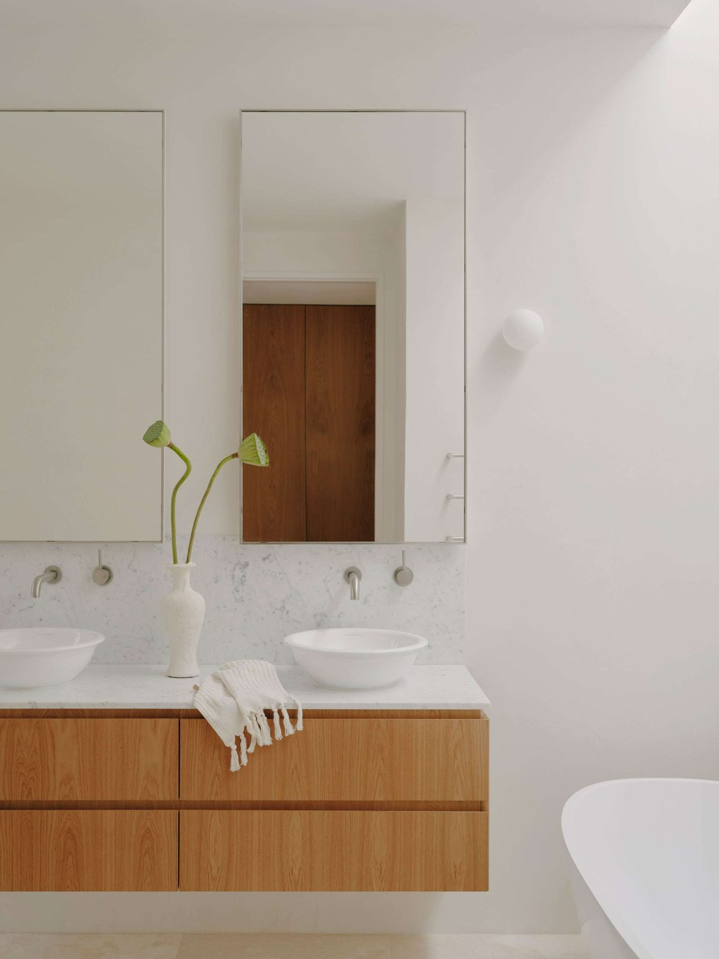 Fitzroy North House by Cera Stribley. Unknown photographer. White bathroom with warm wood vanity, marble splash back and white vase with plant. 