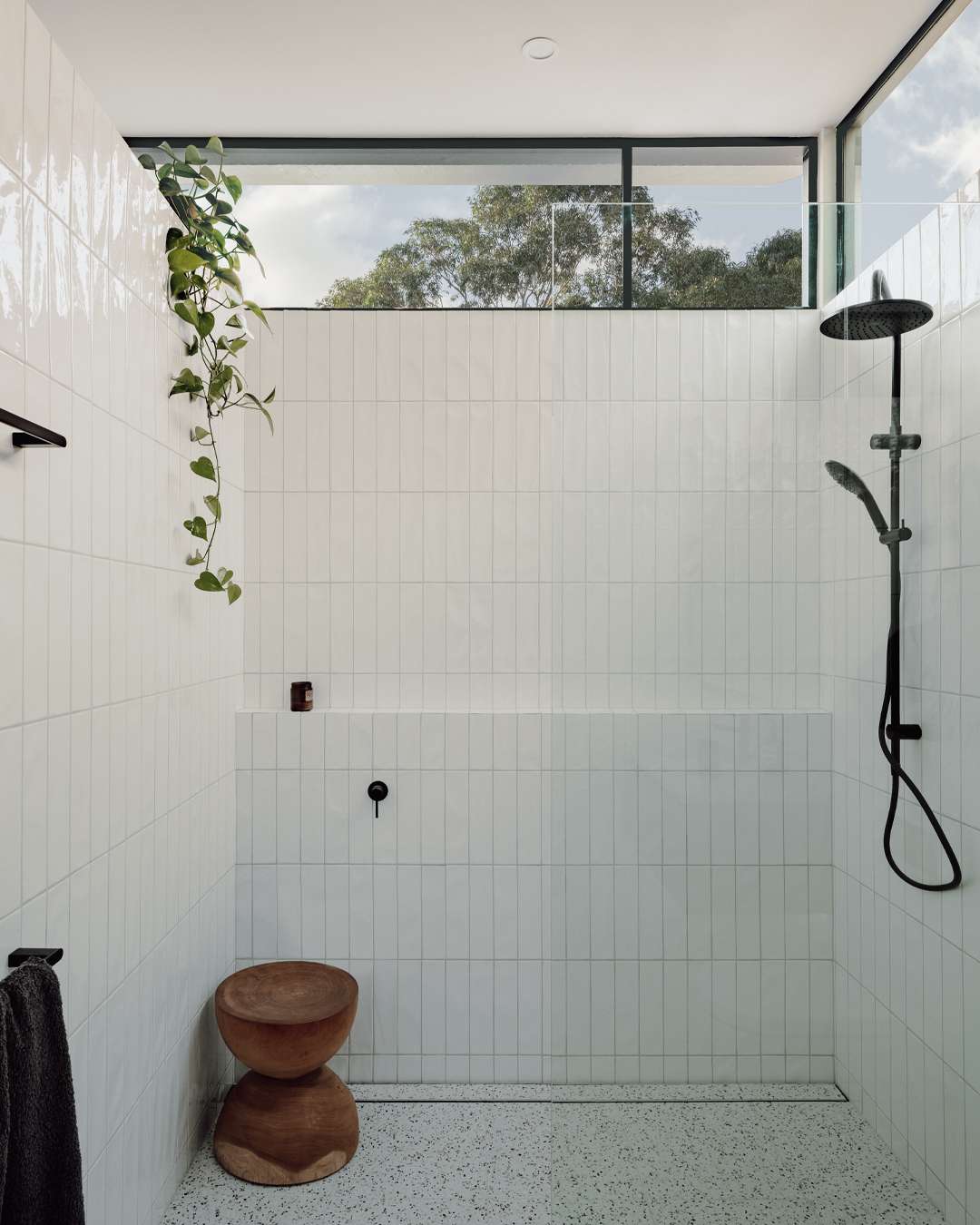 Richmond Terrace by Eckersley Architects. Photography by Dan Preston. Bathroom with floor to ceiling white vertical subway tiles, white tiled floors, a timber stool behind a glass shower screen and black metal windows and fixtures.