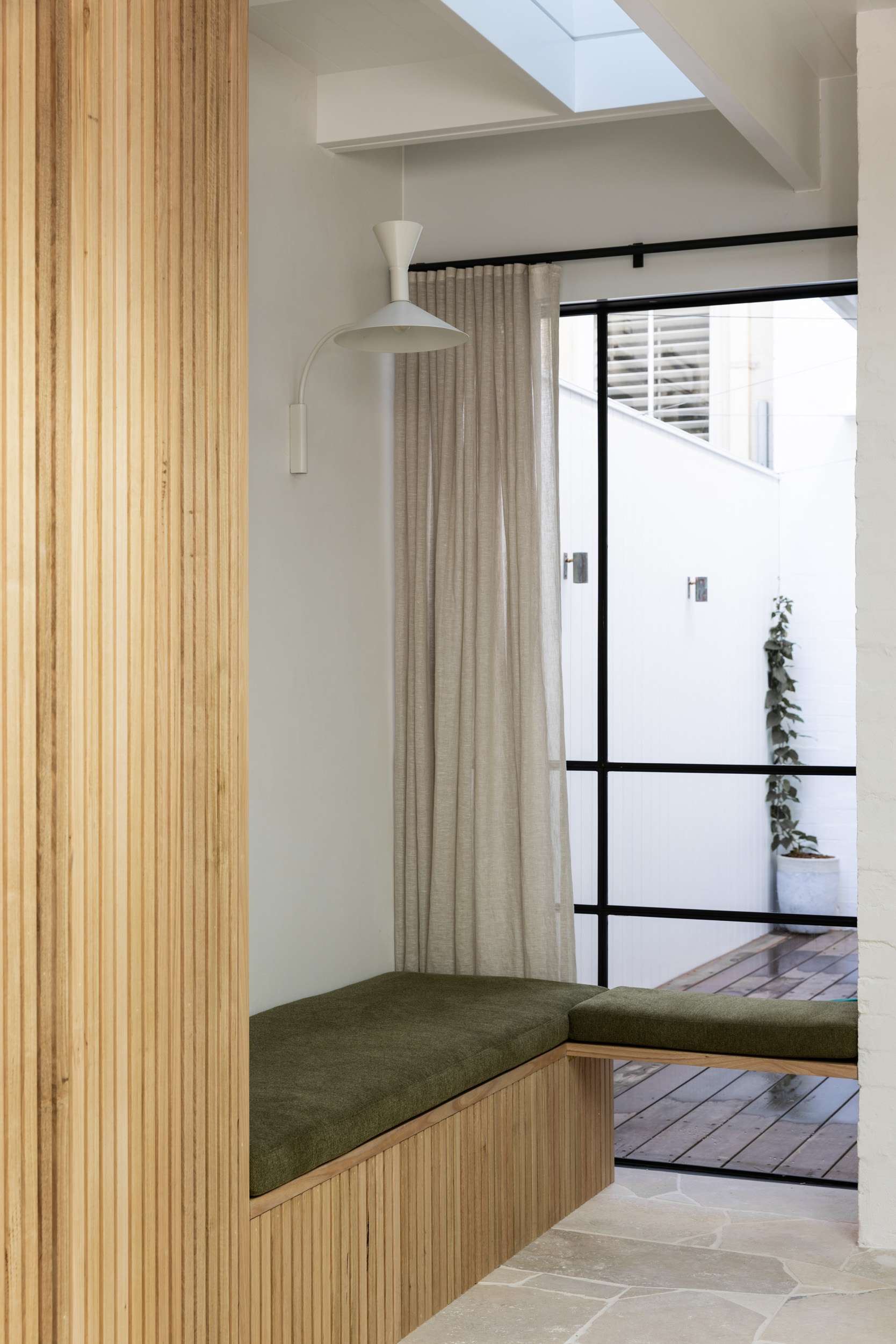 George Humphreys House by Robertson Collectif. Photography by Simon Whitbread. Timber and moss green floating becnh in front of window, looking onto timber decked backyard through black framed grid windows. 