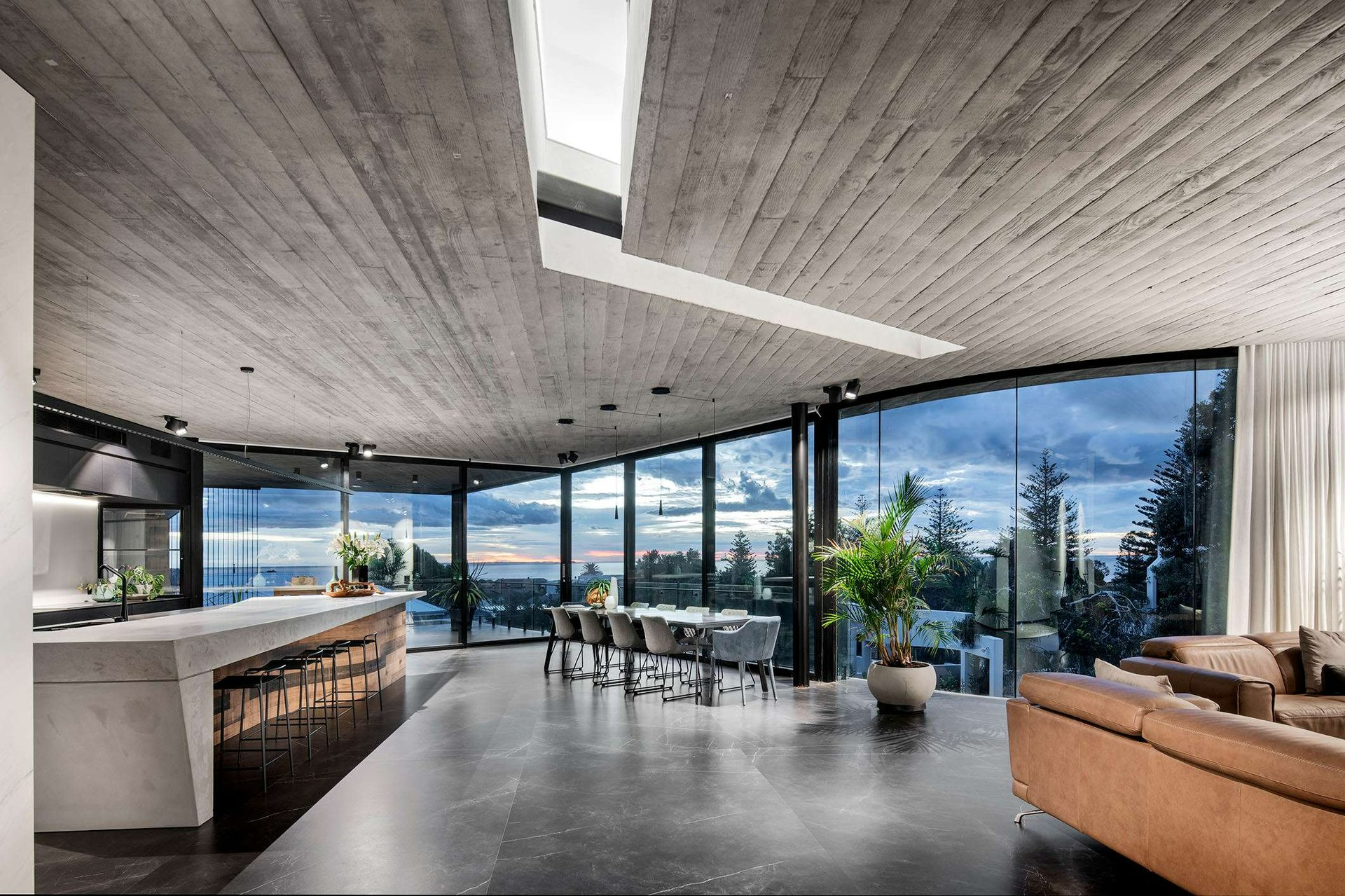 Truro Residence by Hillam Architects. Photography by Joel Barbitta. Open plan kitchen, dining and lving space with dark tiles floors, glass walls and concrete ceiling and island bench.
