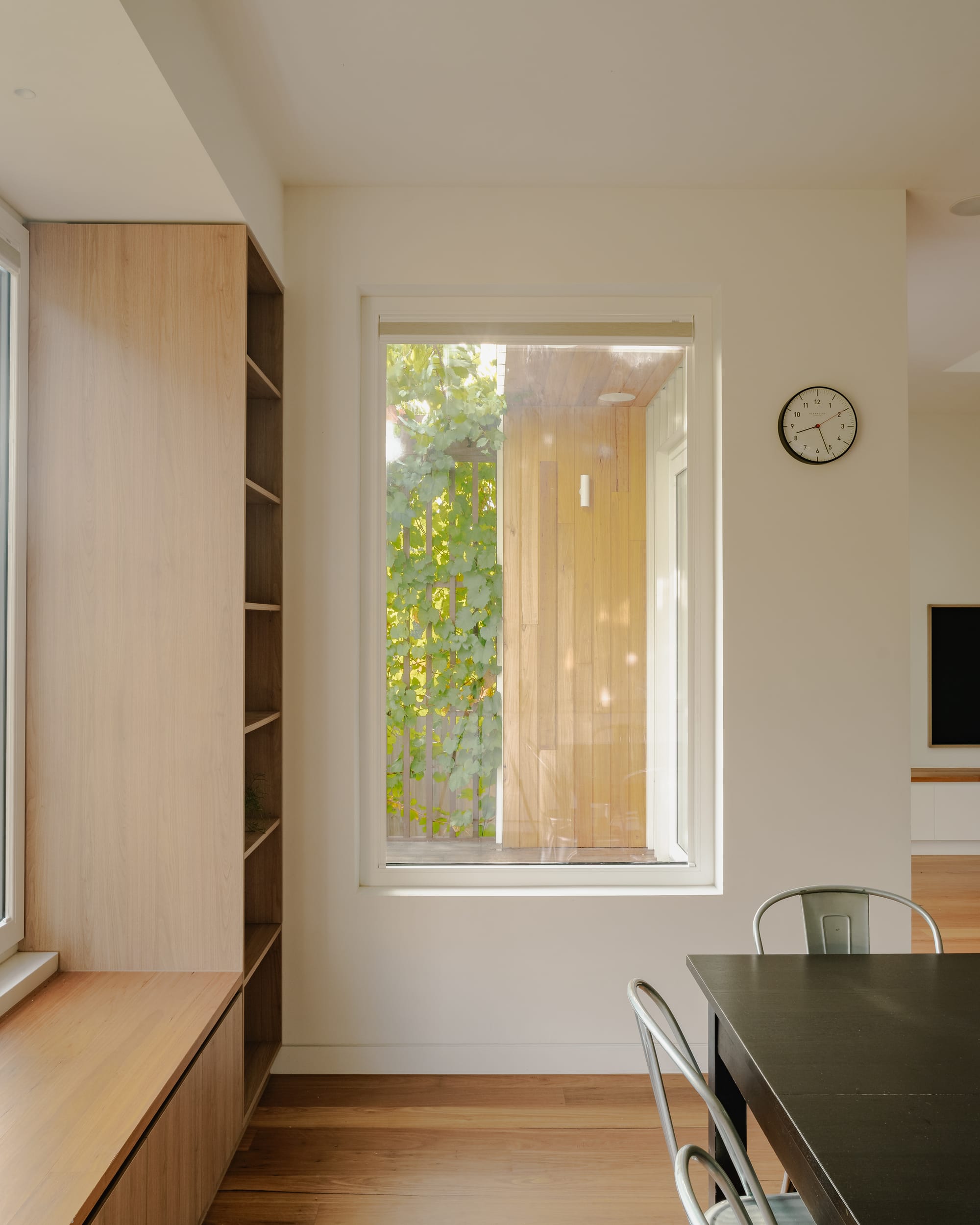 House in Preston by Ashley O'Neill Architects. Photography by Victor Vieaux. Dining space with integrated timber bench seating and storage, designed around windows that over views over rear garden. Black timber dining table with chrome chairs in right foreground. 