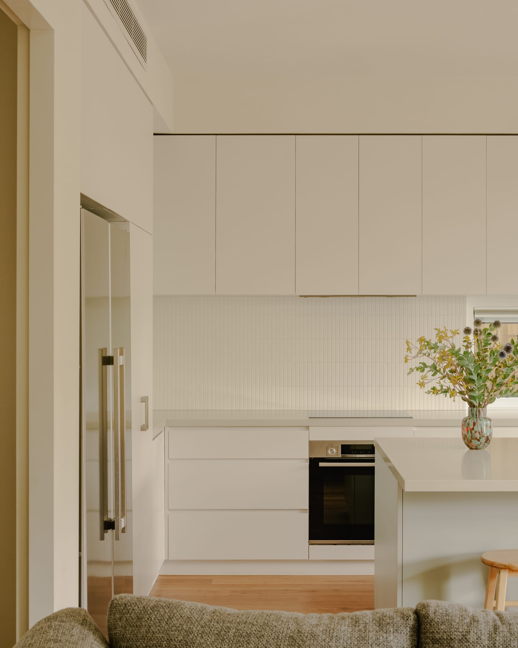 House in Preston by Ashley O'Neill Architects. Photography by Victor Vieaux. Kitchen with timber flooring, simple white cabinetry, finger tile splash back, silver appliances and timber stools. 