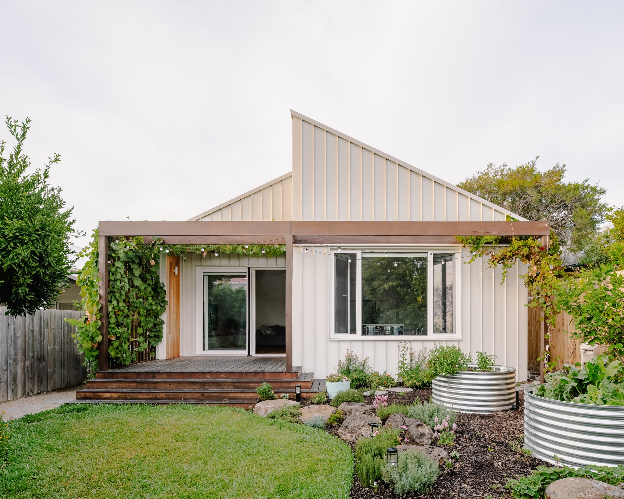 House in Preston by Ashley O'Neill Architects. Photography by Victor Vieaux. Rear facade of cream metal-clad home with large window overlooking garden.