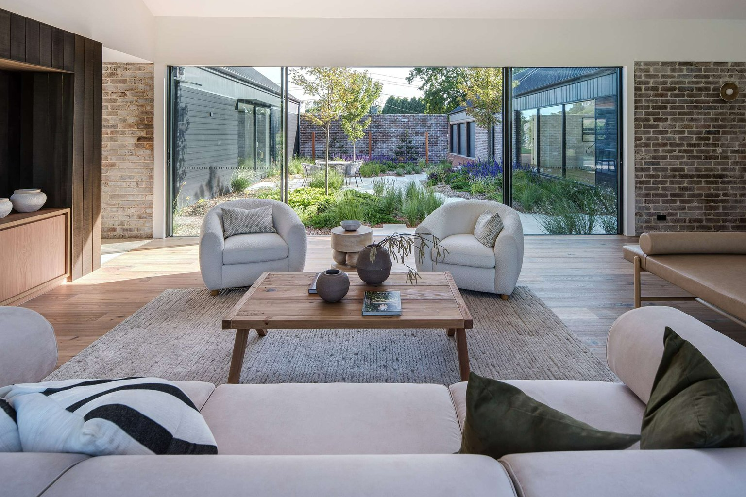 House Forme by AO Design Studio. Photography by Neil Fenelon. Living space with brown brick walls, light timber flooring, white couches and views through full height sliding glass doors onto an interior courtyard space. 
