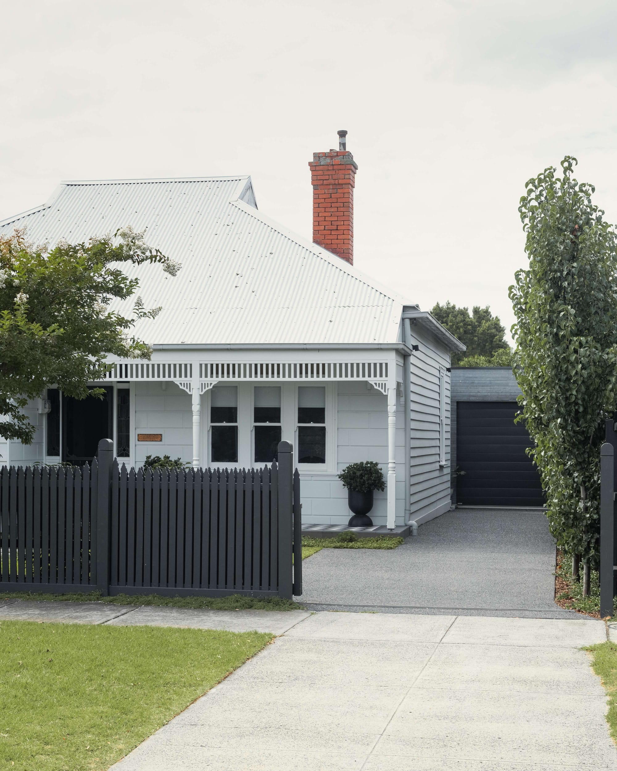 Hughesdale House by Eckersley Architects. Photography by Dan Preston. Front facade of Vicotiran, Federation home with a white pitched tin ceiling, grey walls, black fence and garage door and poured cement driveway. 