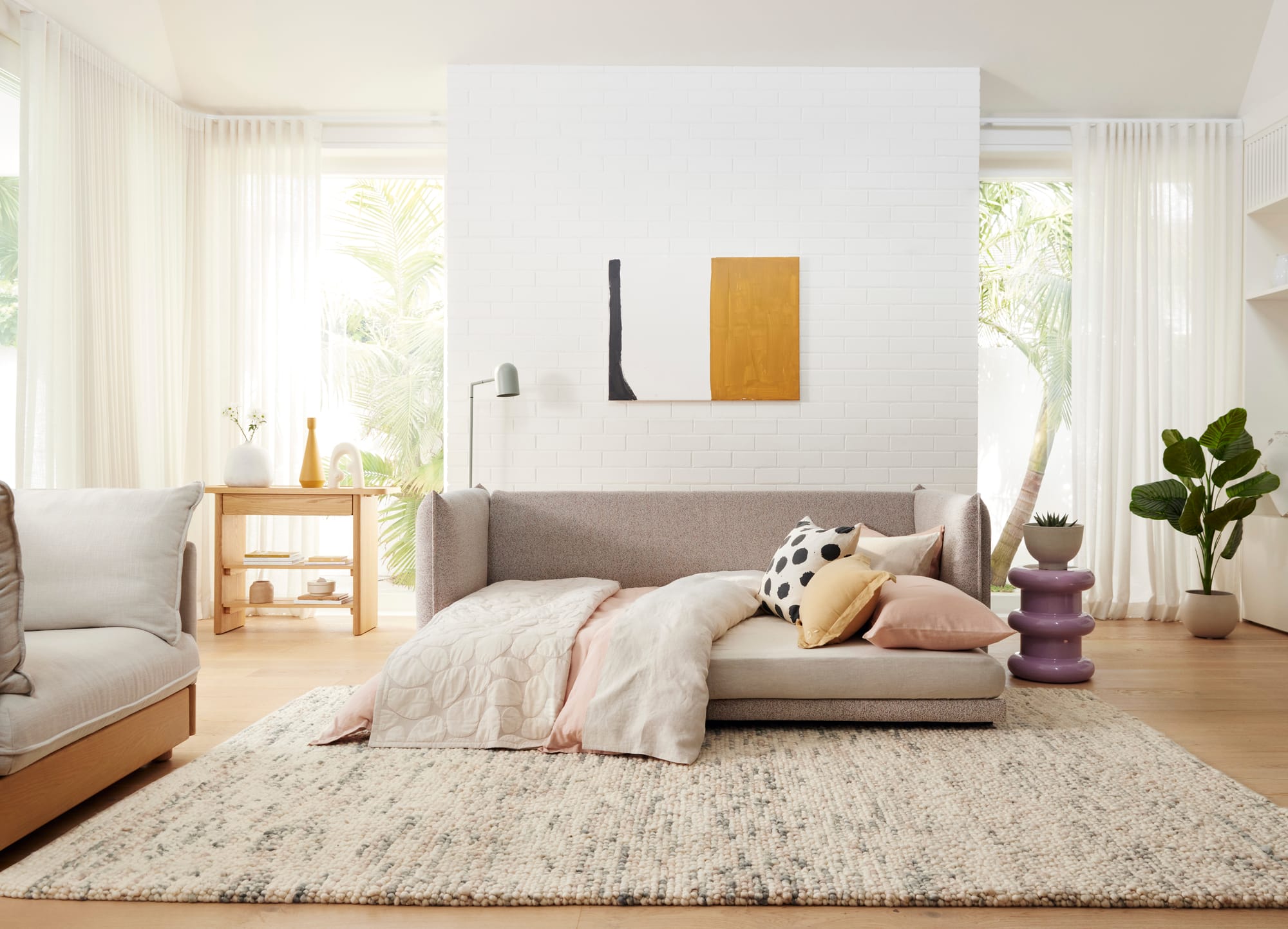 Byron Sofa Bed in Cappuccino by Koala. Light grey sofa bed in space with white brick walls, timber floors, dappled grey floor rug and full height windows overlooking garden.