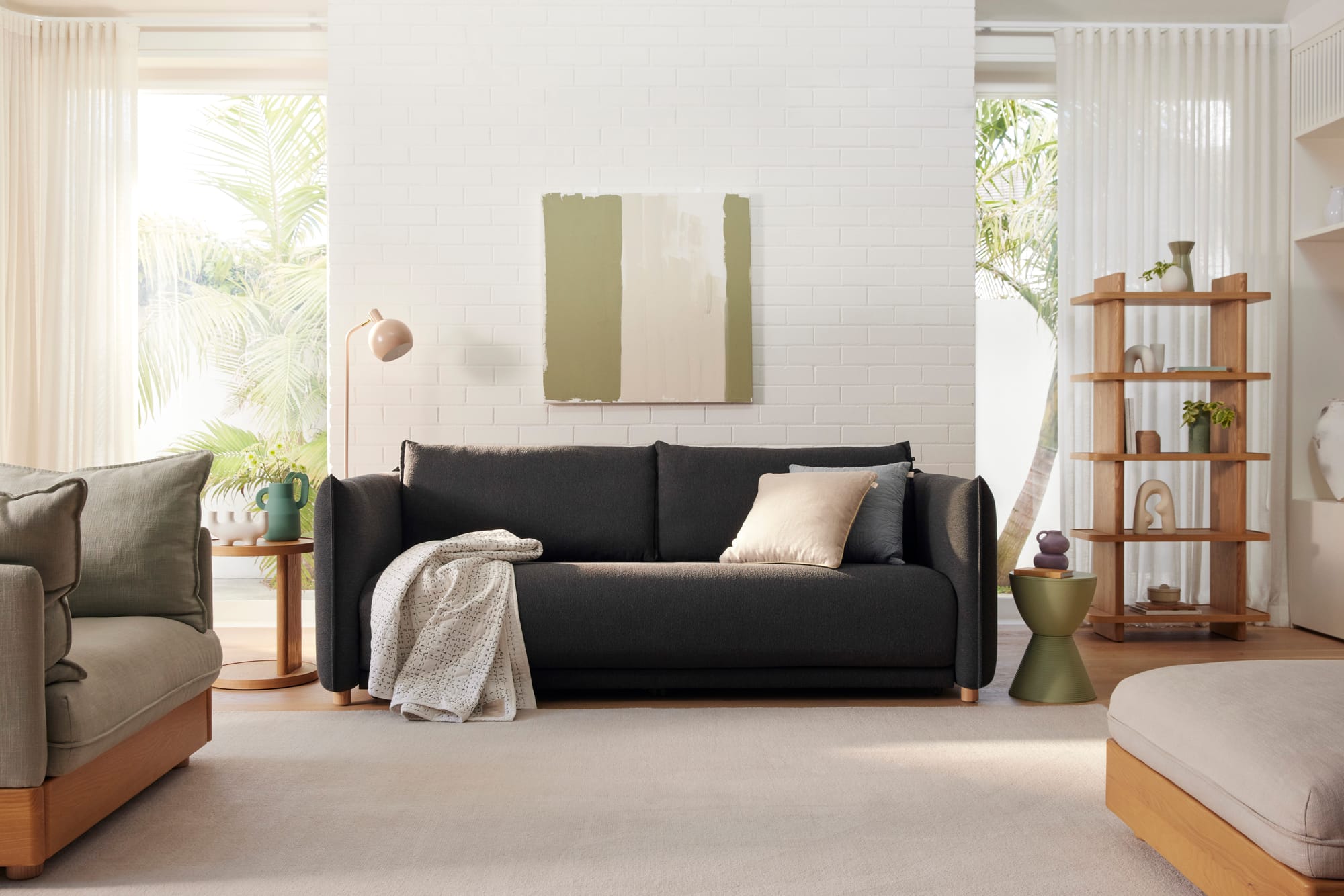 Byron Sofa Bed in Currajong Grey by Koala. Charcoal lounge in living space with white brick walls, light rug, timber furnishings and abstract wall art.