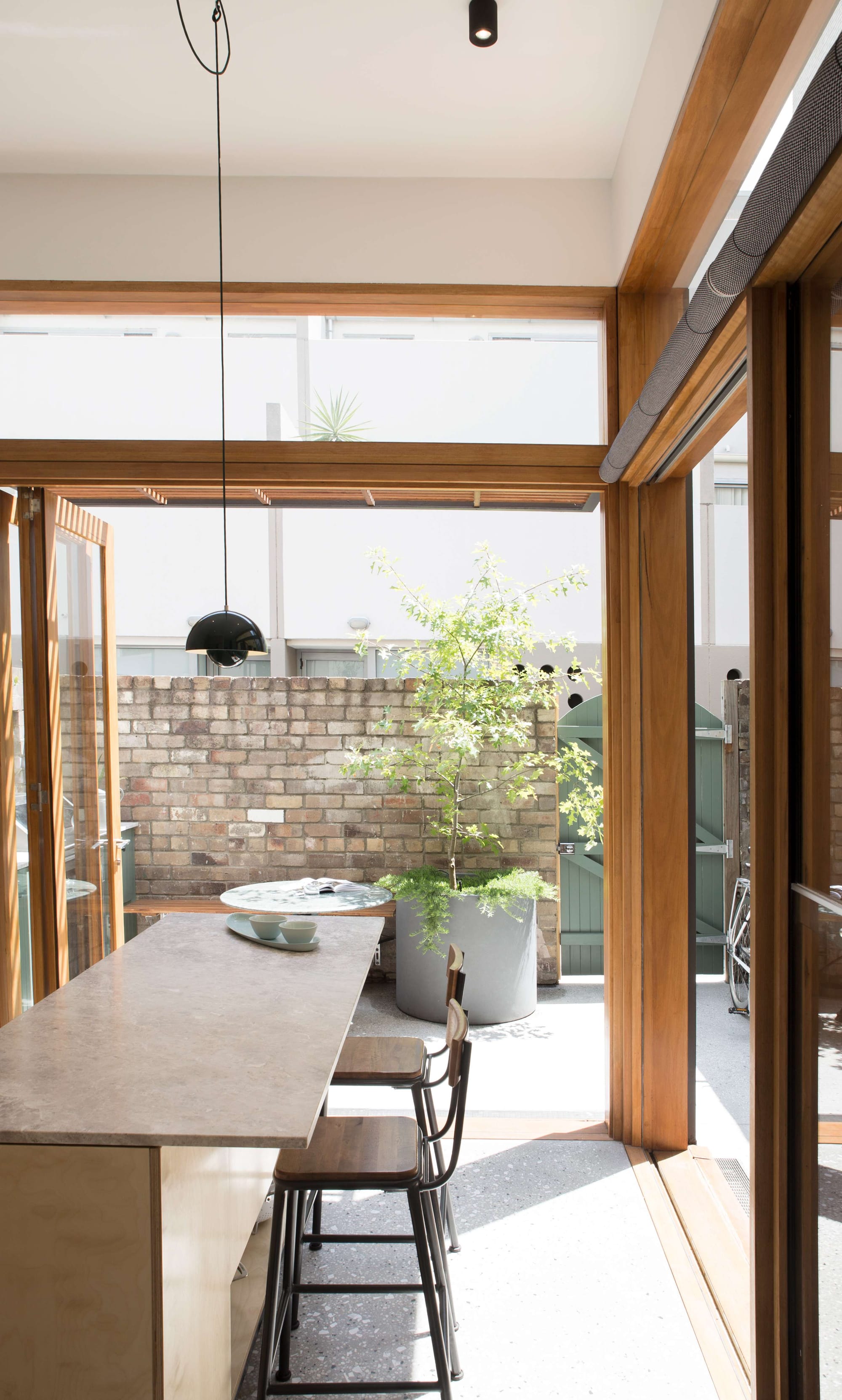 Chippendale Terrace House by Marker Architecture & Design. Photography by Felix Saw. Kitchen space opening onto sunny courtyard via folding timber framed glass doors, with polished concrete flooring inside and out and plywood kitchen cabinetry.