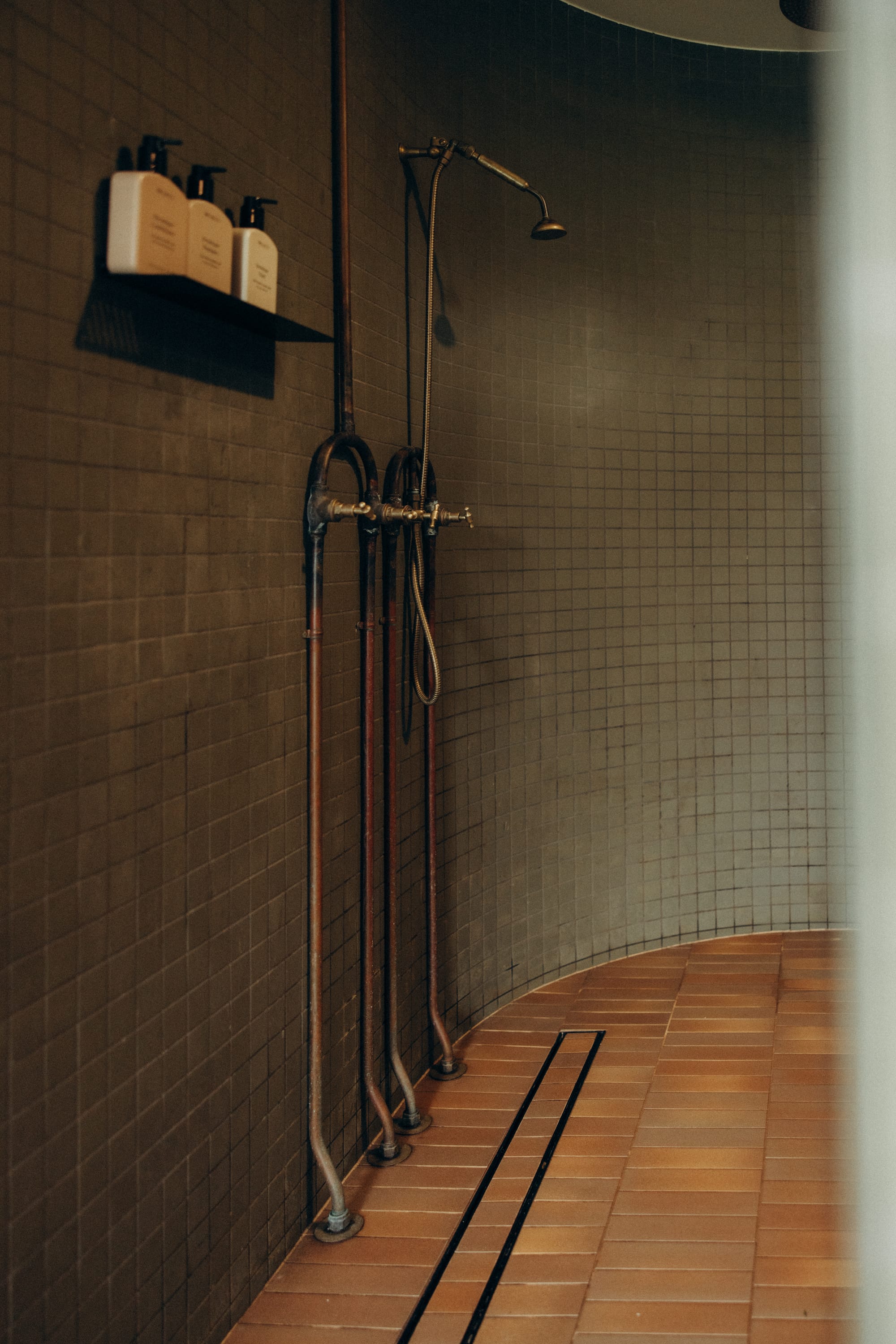Round Hill Retreat by Round Hill Projects x SI.DE Architecture. Photography by Nicci K. Curved wet-room style bathroom with green mosaic wall tiles, terracotta floor tiles and exposed copper plumbing.