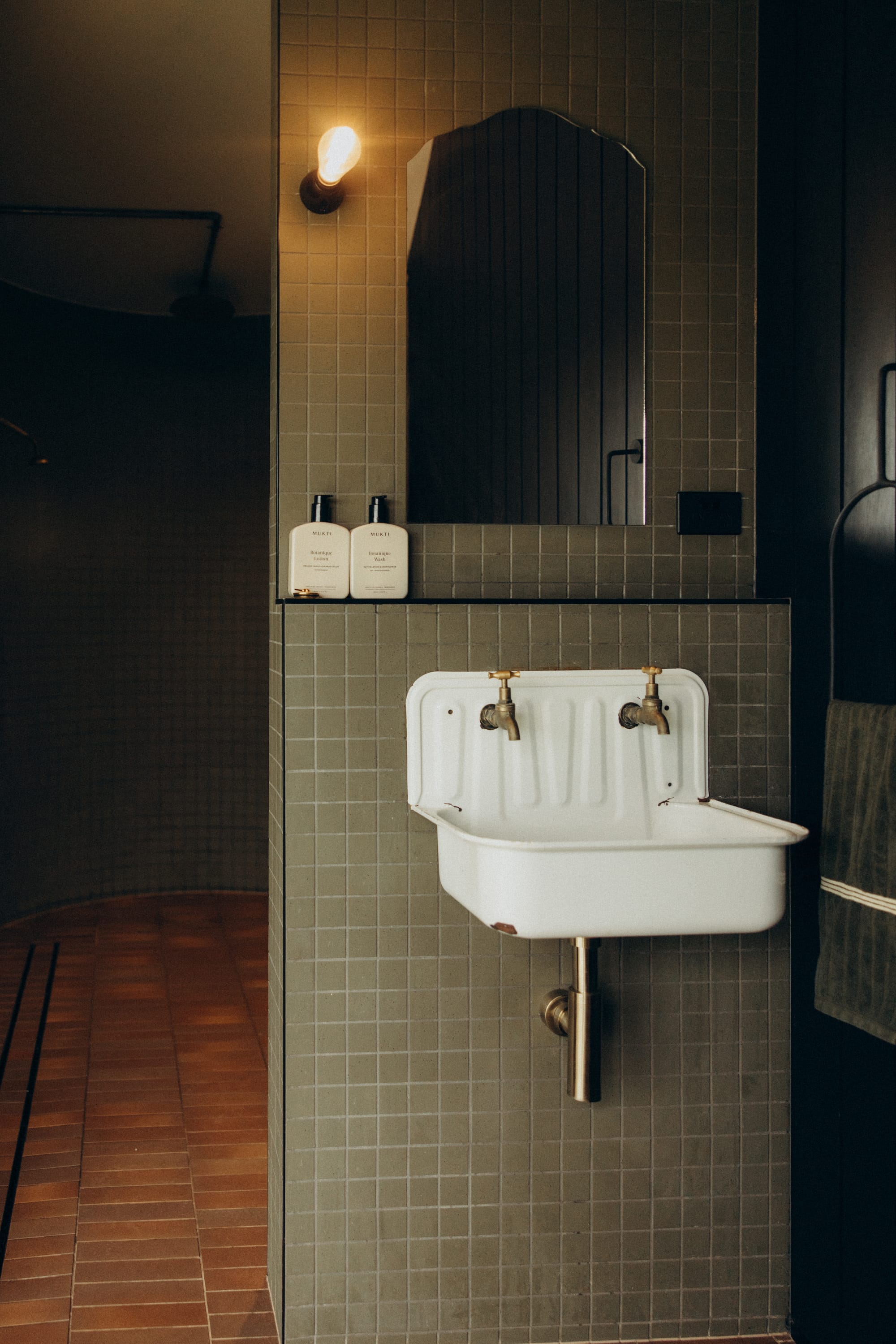 Round Hill Retreat by Round Hill Projects x SI.DE Architecture. Photography by Tim Birch. Bathroom with vintage white wall trough basin, green mosaic wall tiles and terracotta floor tiles.