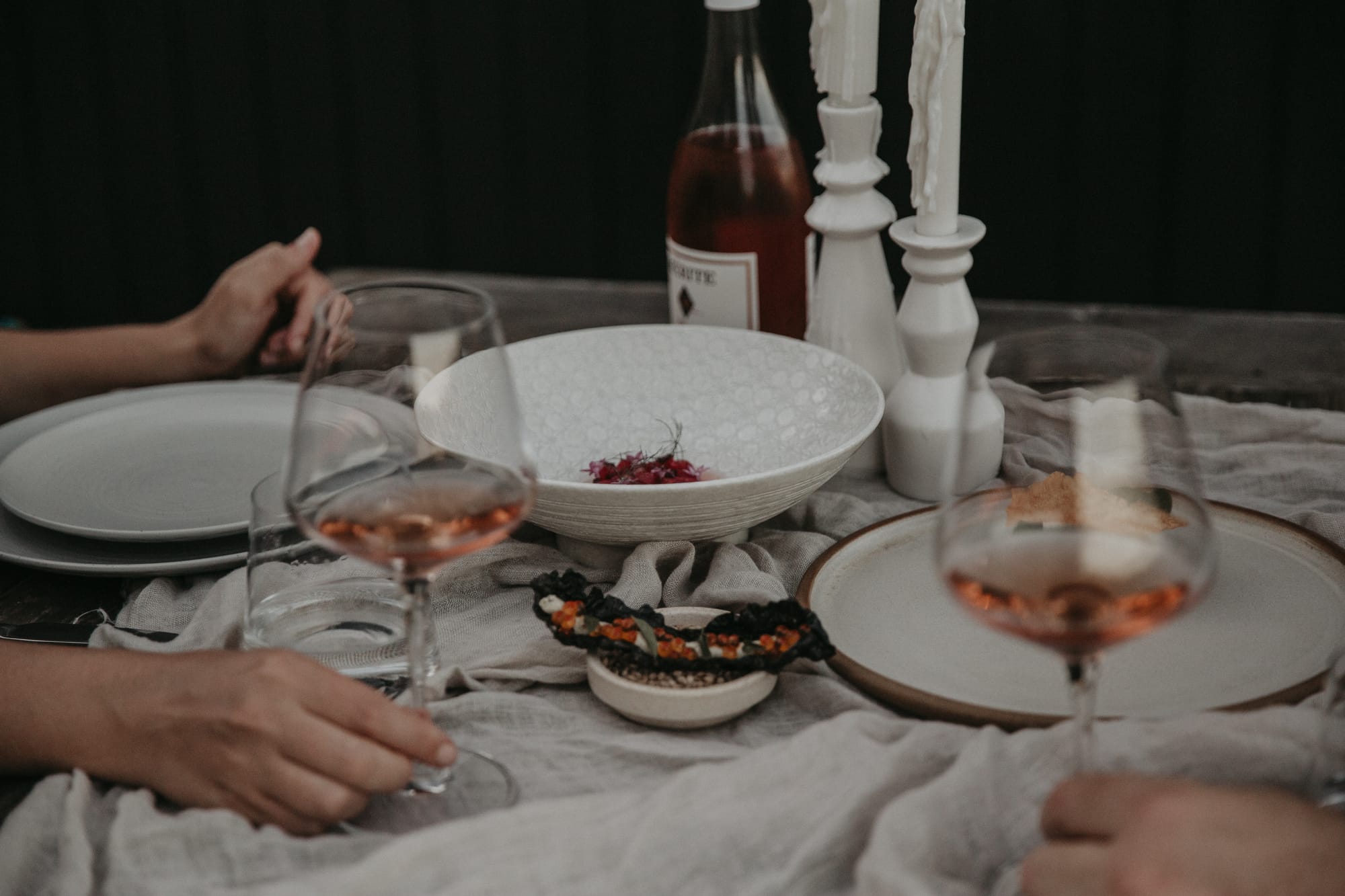 Round Hill Retreat by Round Hill Projects x SI.DE Architecture. Photography by Yani Rae. Table spread with light grey linen tablecloth, white and grey plates, glasses with pink wine and white candle holders.