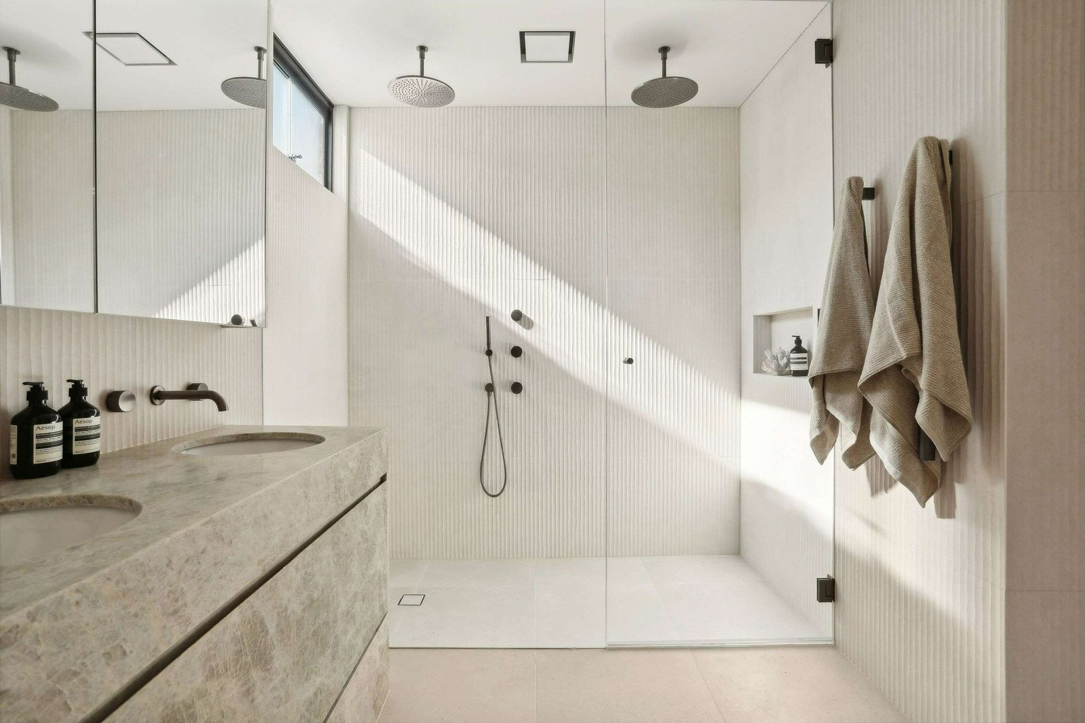 Sunset Calling, Dover Heights by BJB Architects. Photography by Core Photography Australia.  Bathroom wet room with large double shower with beige wall tiles and white floor tiles and a grey marbled counter with mirror. 