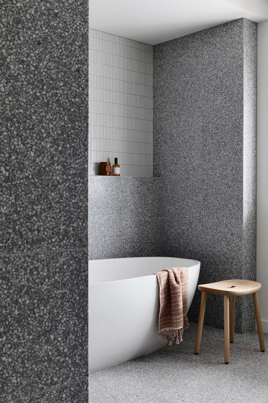 McNamara House by Tom Roberston Architects. Photography by Derek Swalwell. Wet room bathroom with free standing white bath with timber stool, with grey speckled wall and floor tiles.