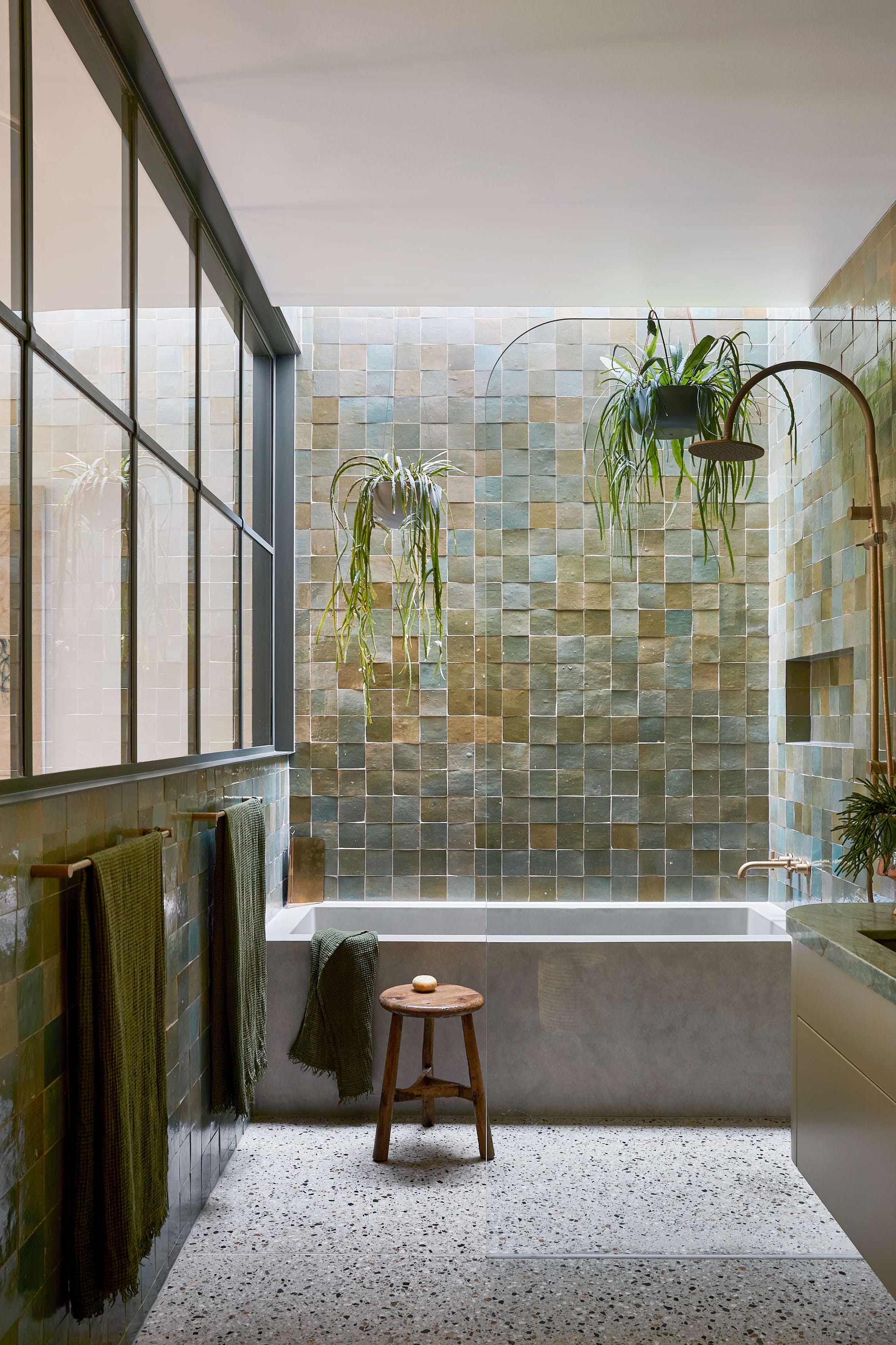 Fabrica by mcmahon and nerlich. Photography by Shannon McGrath. Bathroom with concrete floors and textured wall tiling in various shades of green, with a concrete bath and a timber stool.