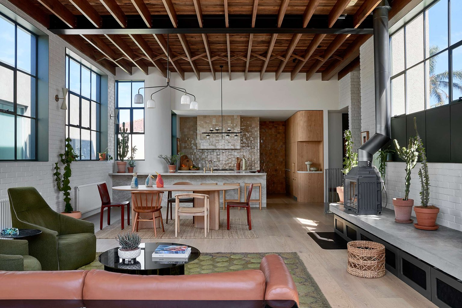 Fabrica by mcmahon and nerlich. Photography by Shannon McGrath. Eclectic residential space with exposed beams, timber floors, white brick walls, black grid windows, concrete finishes, mosaic tiled splashback and furnishings in shades of green, red, black and brown. 