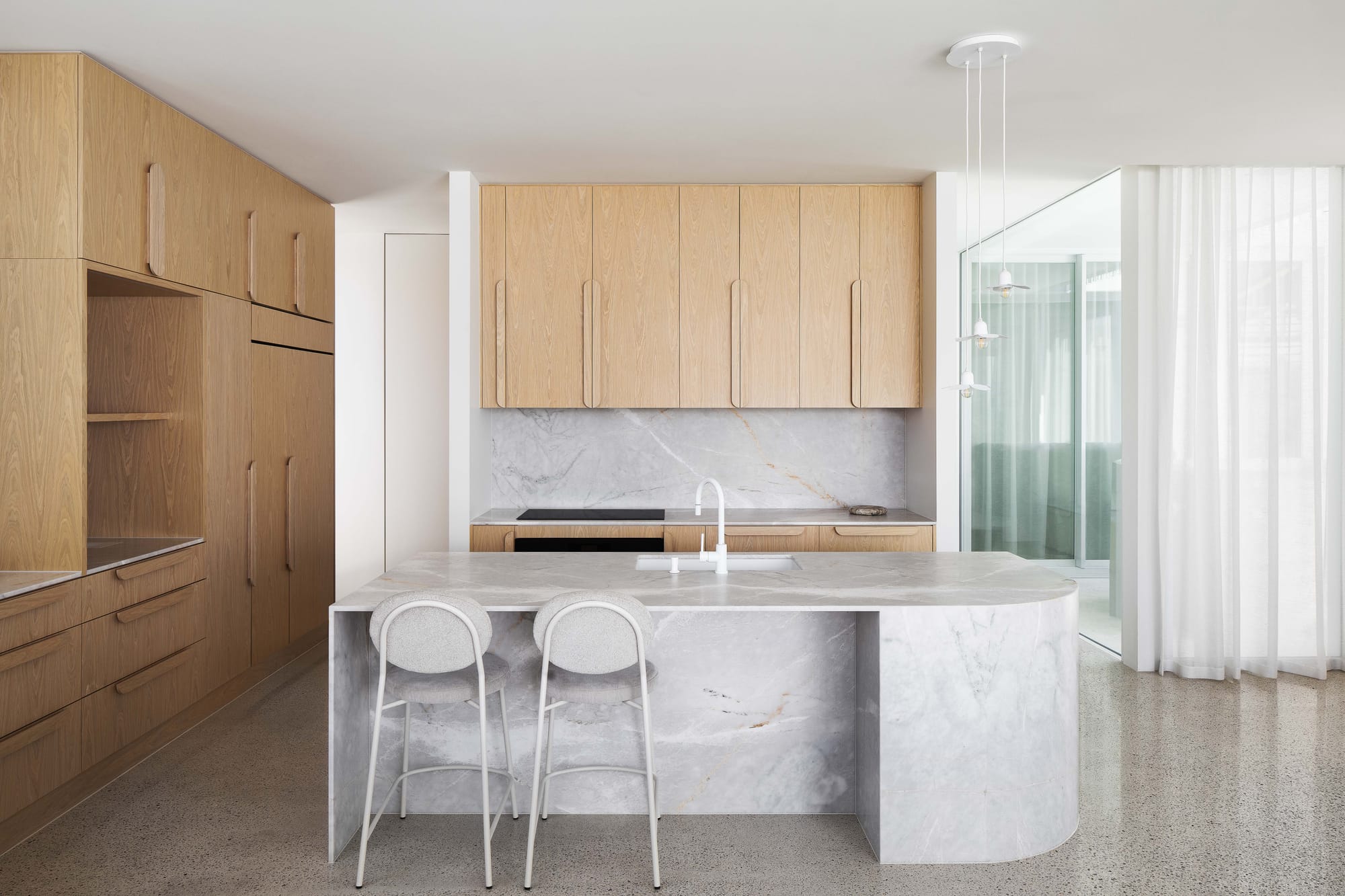 Alba House by Taouk Architects. Photography by Emily Bartlett. Living space with lime washed beige walls, modular grey couch, fluffy white floor rug, polished concrete floors and large glass doors. 