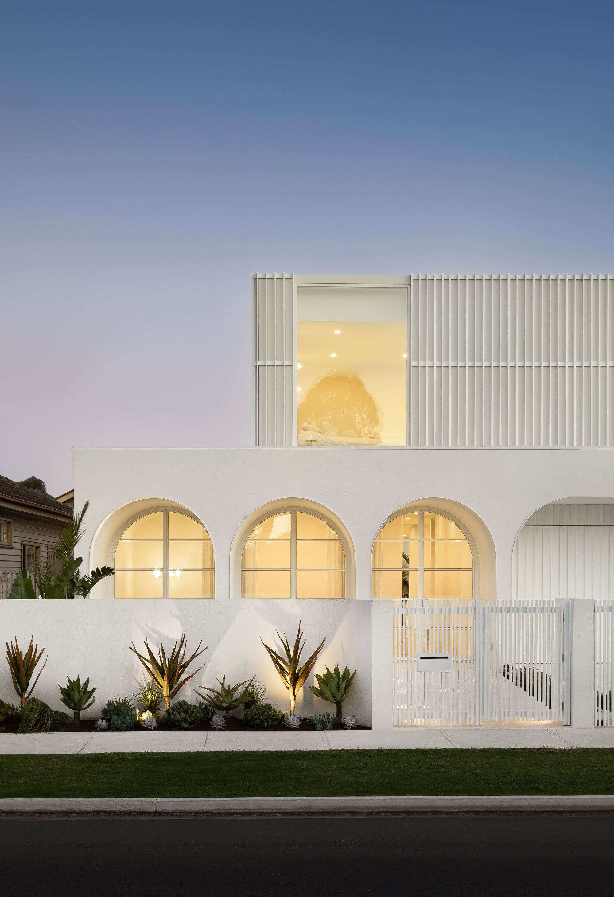Alba House by Taouk Architects. Photography by Emily Bartlett. Facade of white double-storey home with curved windows and fluted exterior paneling. 
