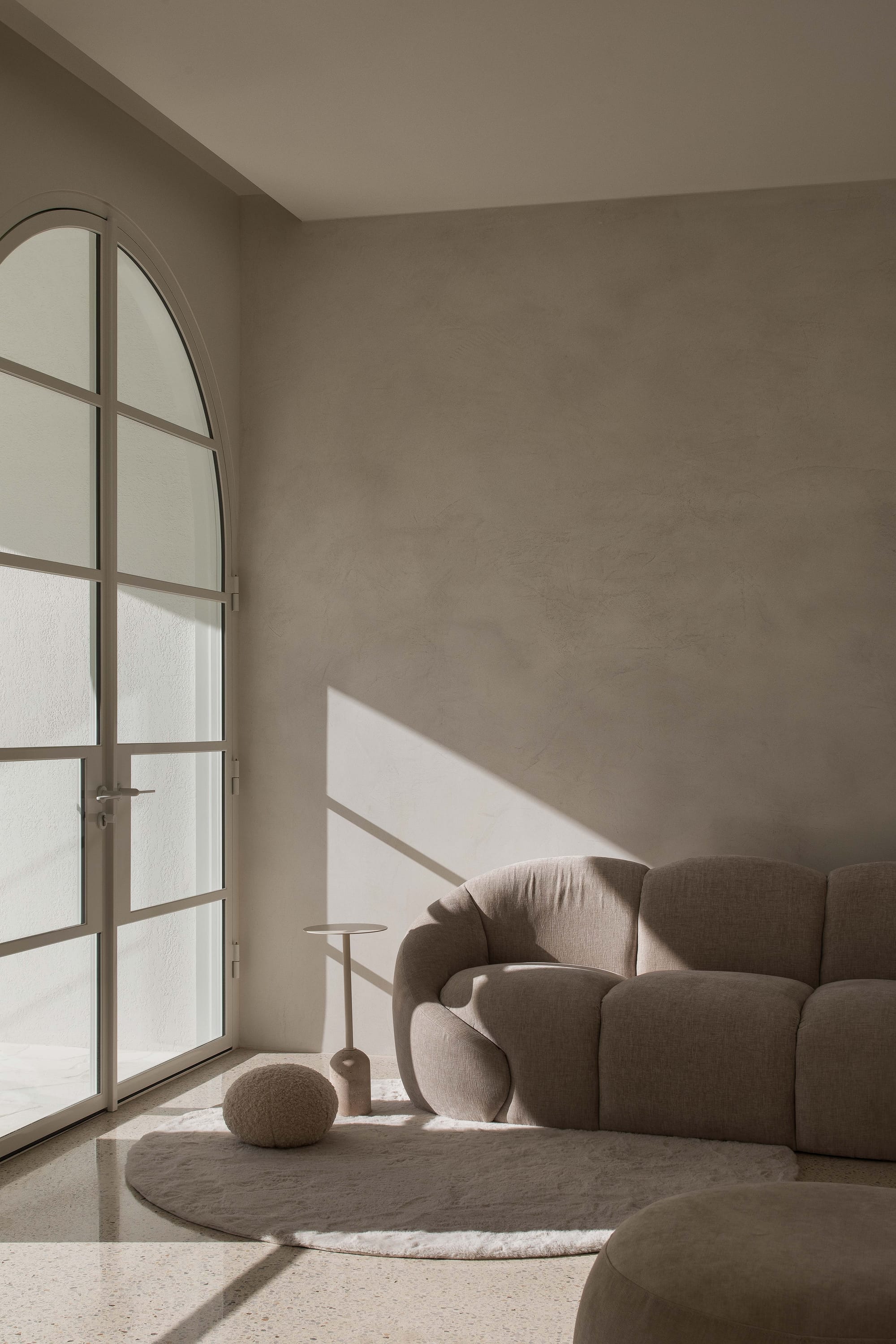 Alba House by Taouk Architects. Photography by Emily Bartlett. Living space with lime washed beige walls, modular grey couch, fluffy white floor rug, polished concrete floors and large glass doors. 