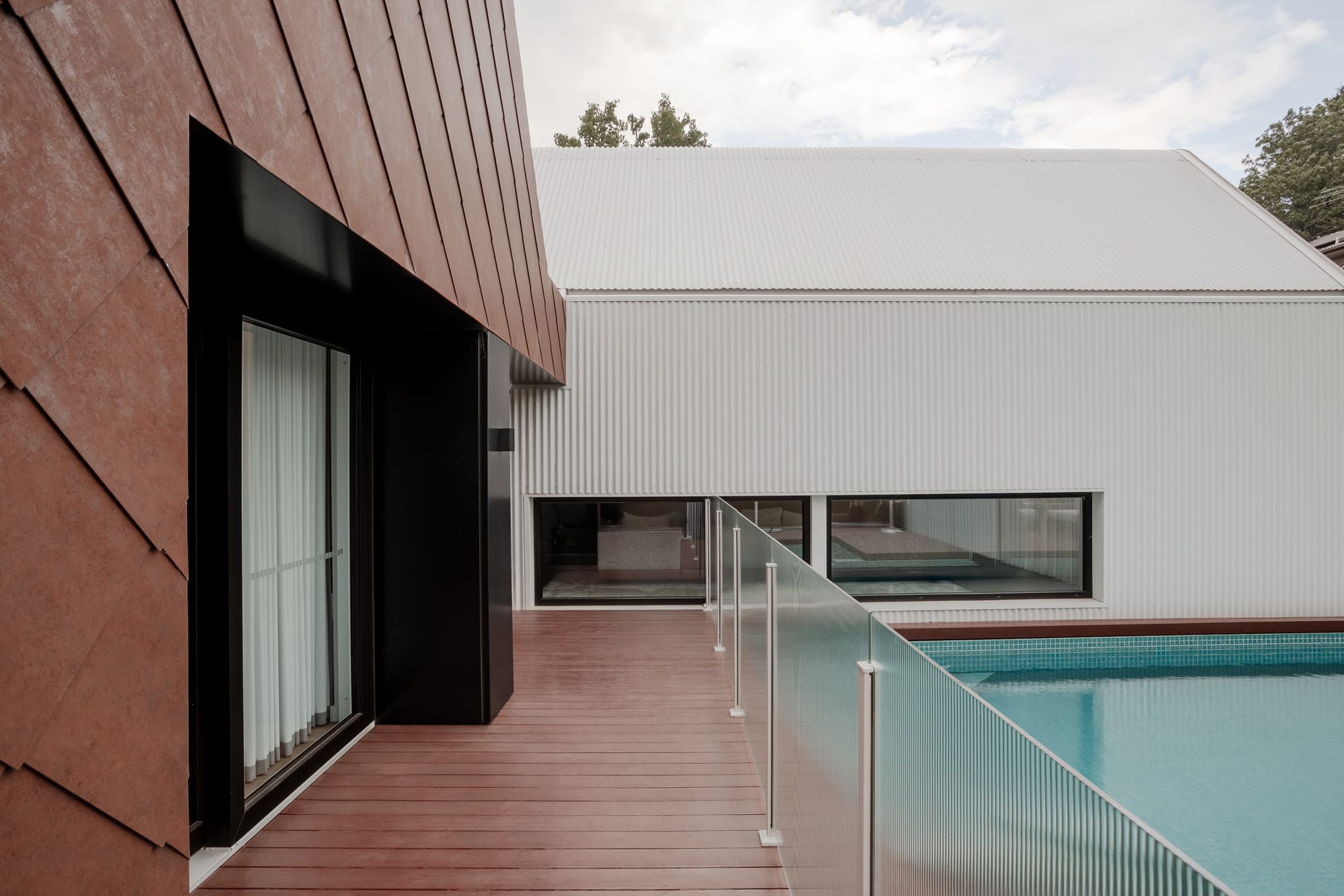 TREE HOUSE by R Architecture. Photography by CM Photography. Timber decking with glass fence running alongside pool with blue tiling.