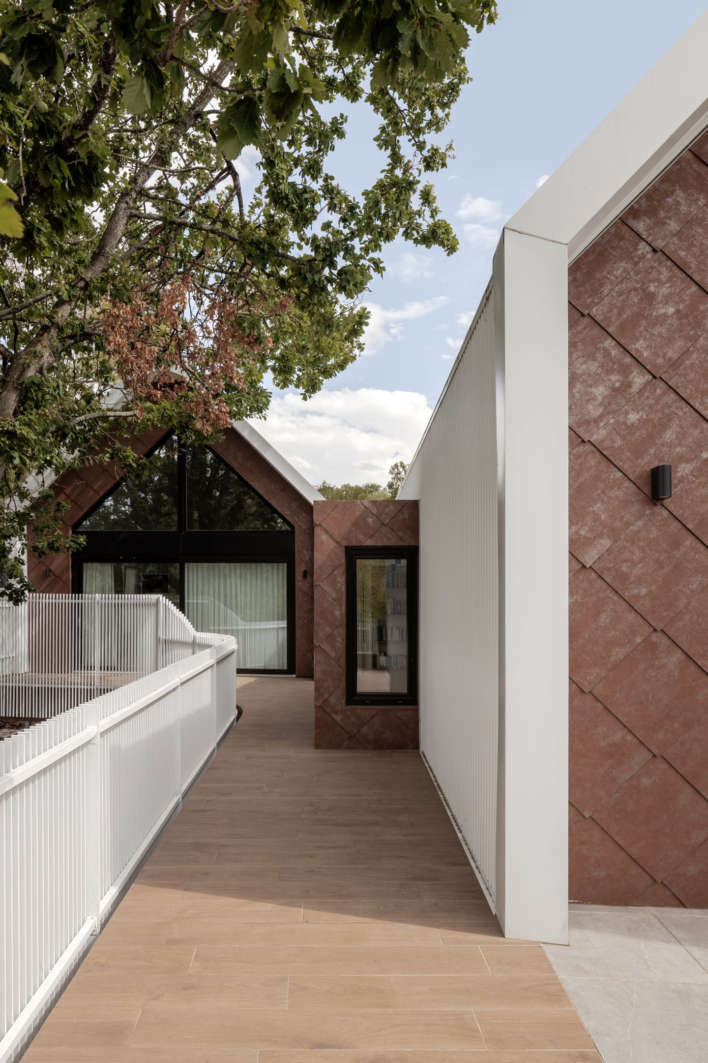 TREE HOUSE by R Architecture. Photography by CM Photography. External walkway with timber-look pavers, white fencing and terracotta, metal clad exterior. 