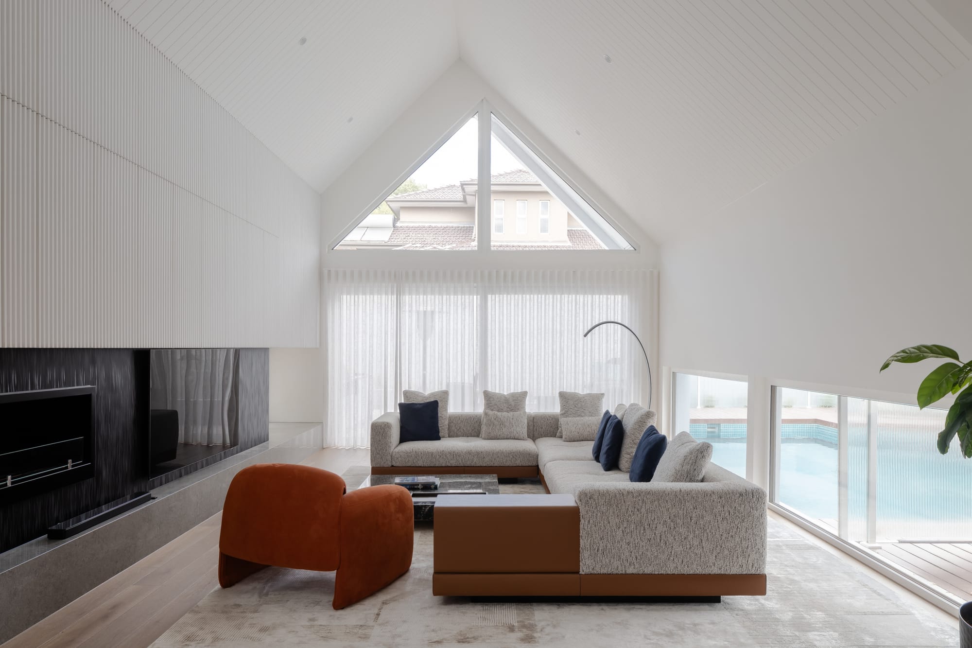 TREE HOUSE by R Architecture. Photography by CM Photography. Open plan living room with white walls, pitched roof and glass windows looking at the swimming pool.