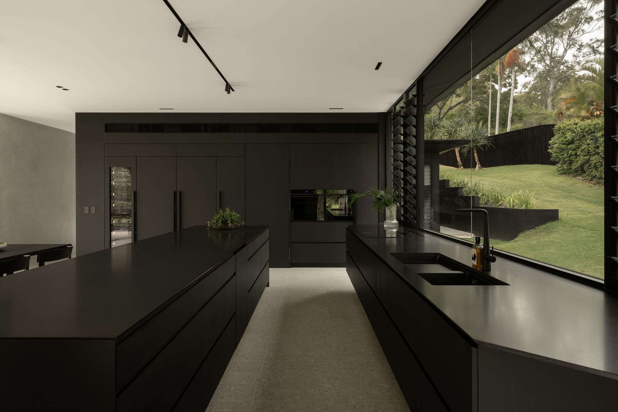 Blackwood Doonan by Sarah Waller Architects. Interior of the kitchen showing black cabinetry and a large window showing the backyard.