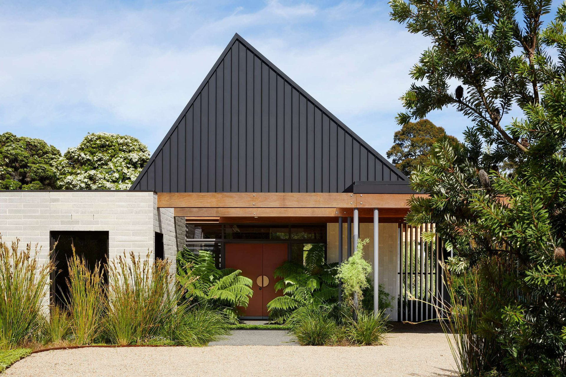 Mt Eliza by BENT Architecture. Photography by Tajana Plitt. House with high black pitched roof with large ferns and grass plants by front door. 