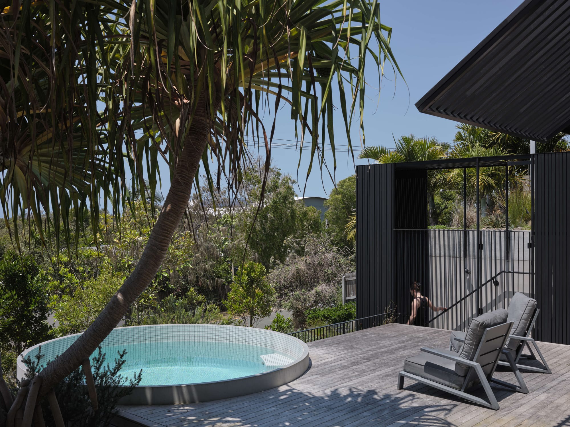 Blok Peregian by Blok Modular. Photography by Christopher Frederick Jones. Weathered timber deck with round white tiled pool, grey deck chairs and views over native bushland.