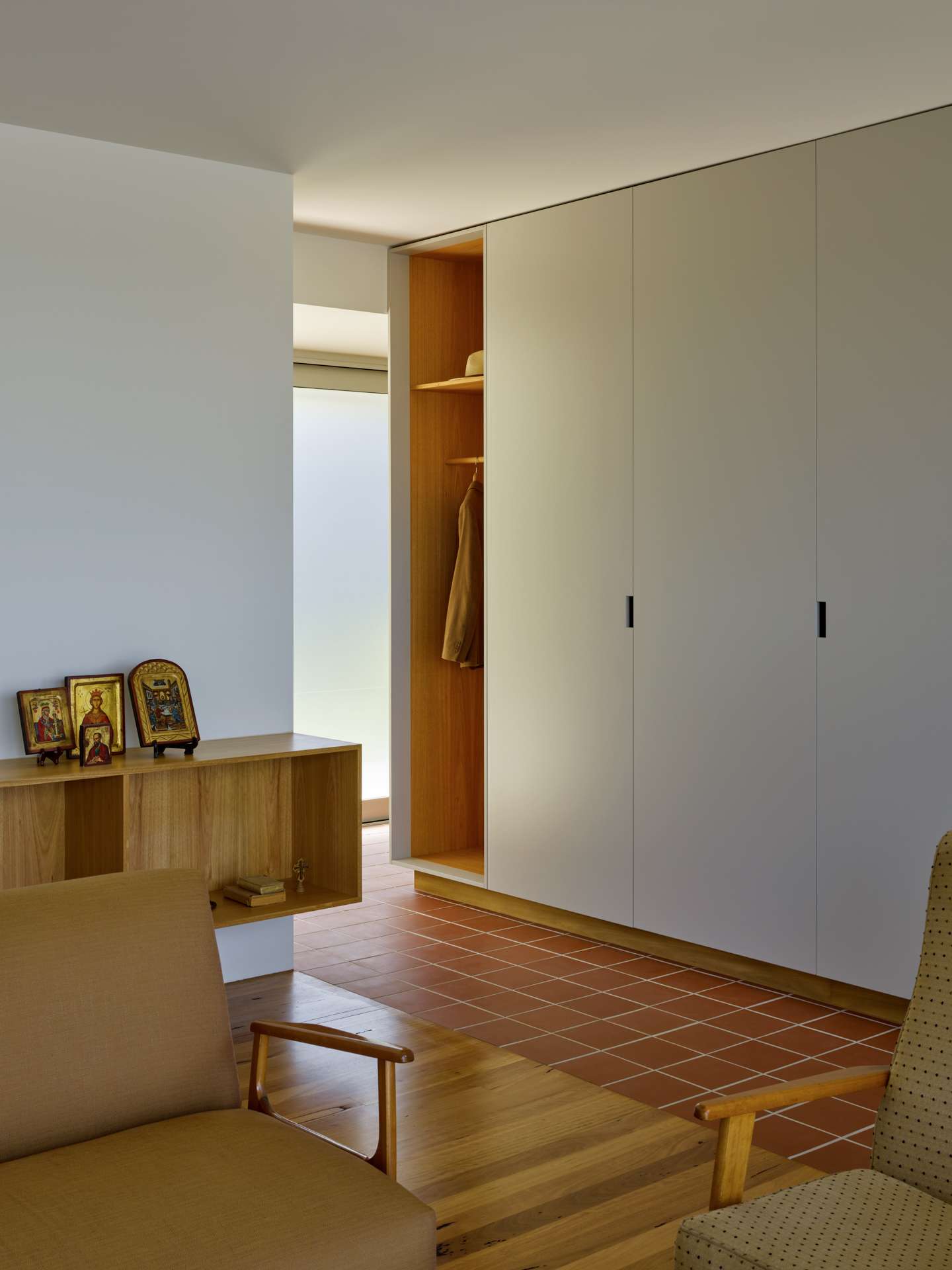 Blok Peregian by Blok Stafford Heights. Photography by Christopher Frederick Jones. Living space with white cabinetry, terracotta floor tiles, timber flooring and mid-century modern armchairs.