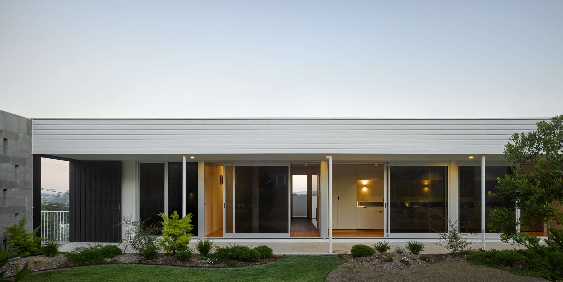 Blok Peregian by Blok Stafford Heights. Photography by Christopher Frederick Jones. Facade of pavilion home with full height glass sliding doors, windows, a white roof and a tiled patio.