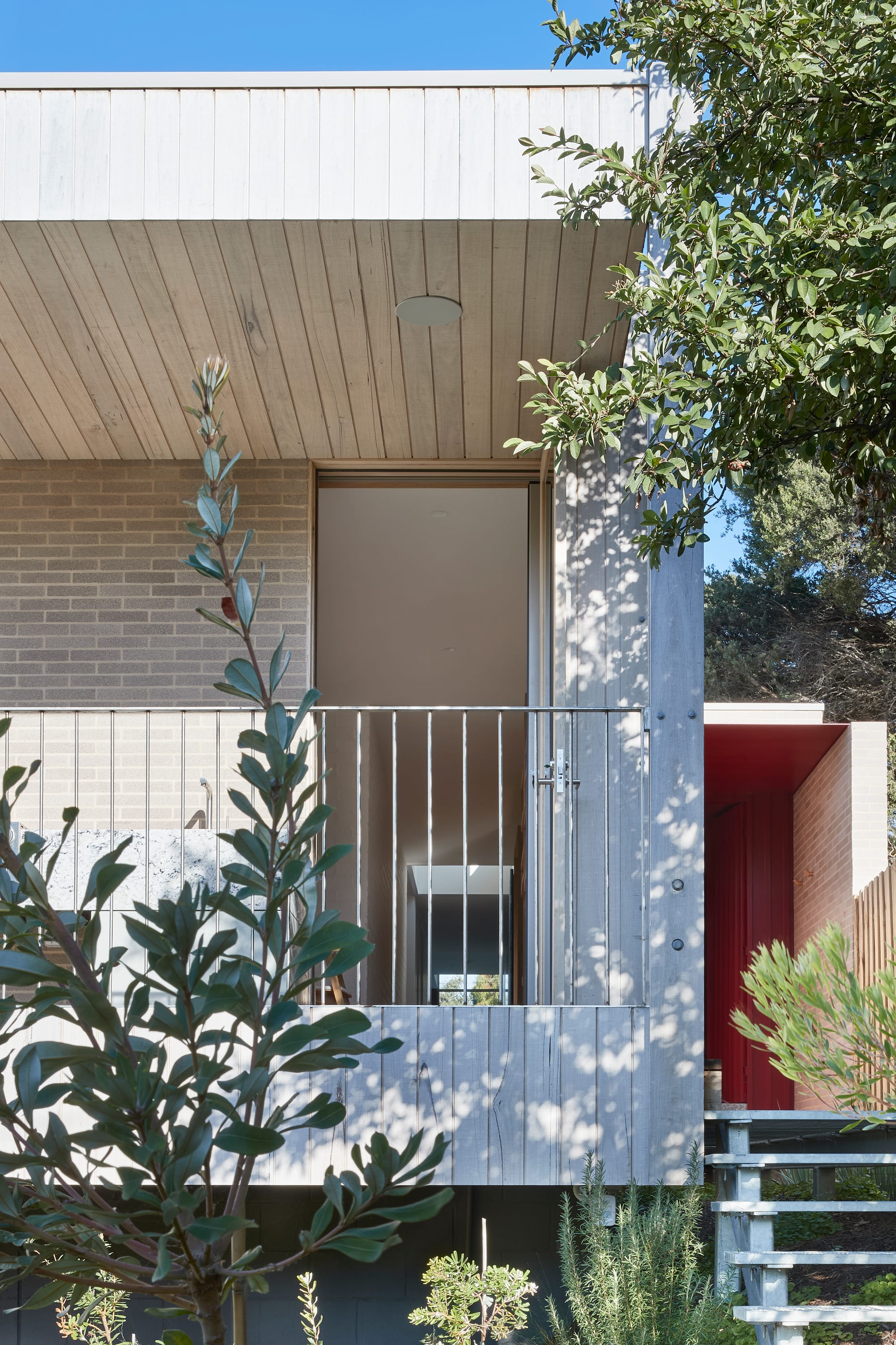 The Blairgowrie Beach Club by Bower Architecture & Interiors. Photography by Shannon McGrath. Close up view of a house with balcony with wooden cladding and entrance on side.