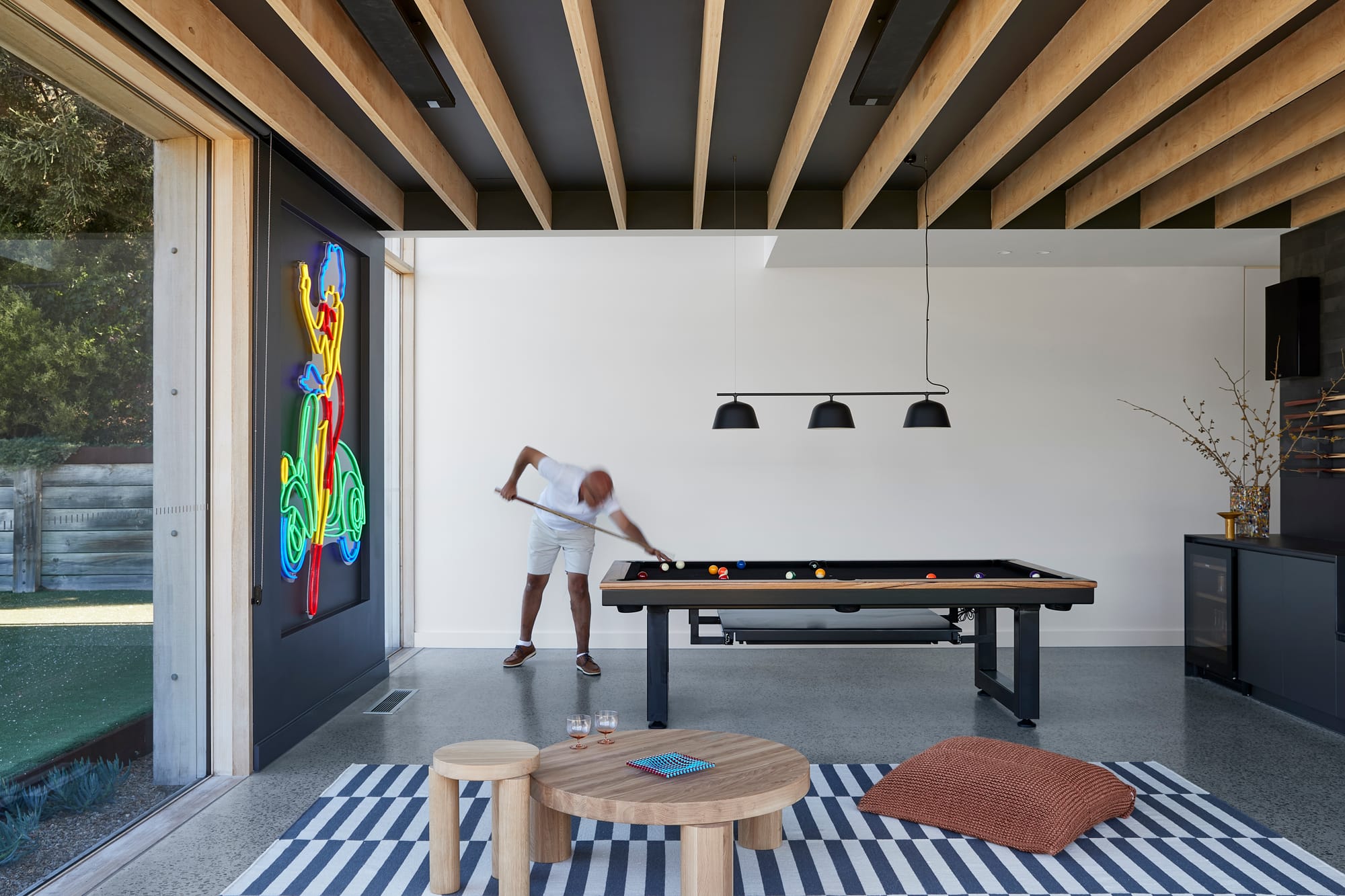 The Blairgowrie Beach Club by Bower Architecture & Interiors. Photography by Shannon McGrath. A man playing pool in a room with neon sign of vespa against the wall.