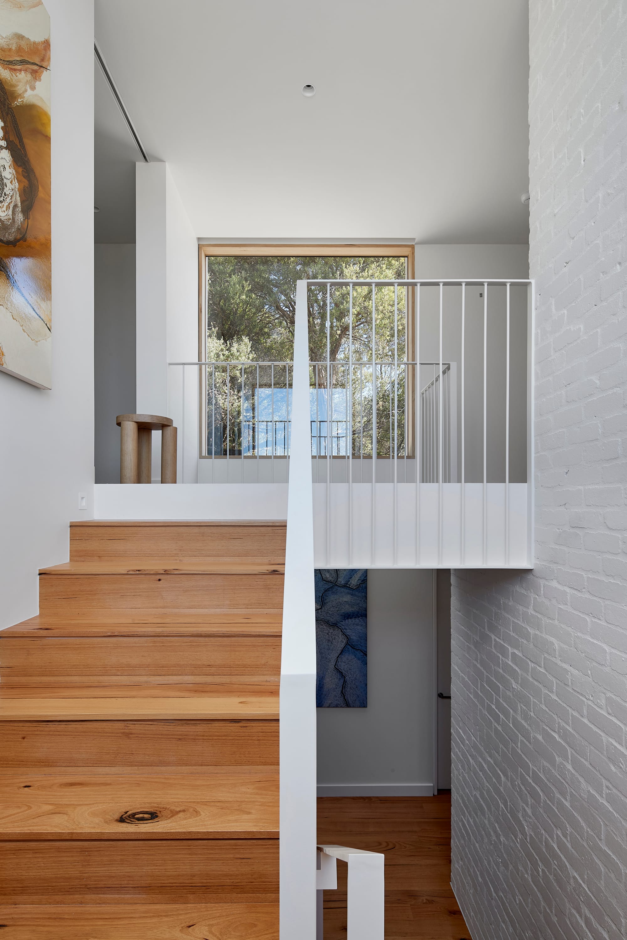 The Blairgowrie Beach Club by Bower Architecture & Interiors. Photography by Shannon McGrath. Wooden staircase with white metal railing with frames hanged on wall.