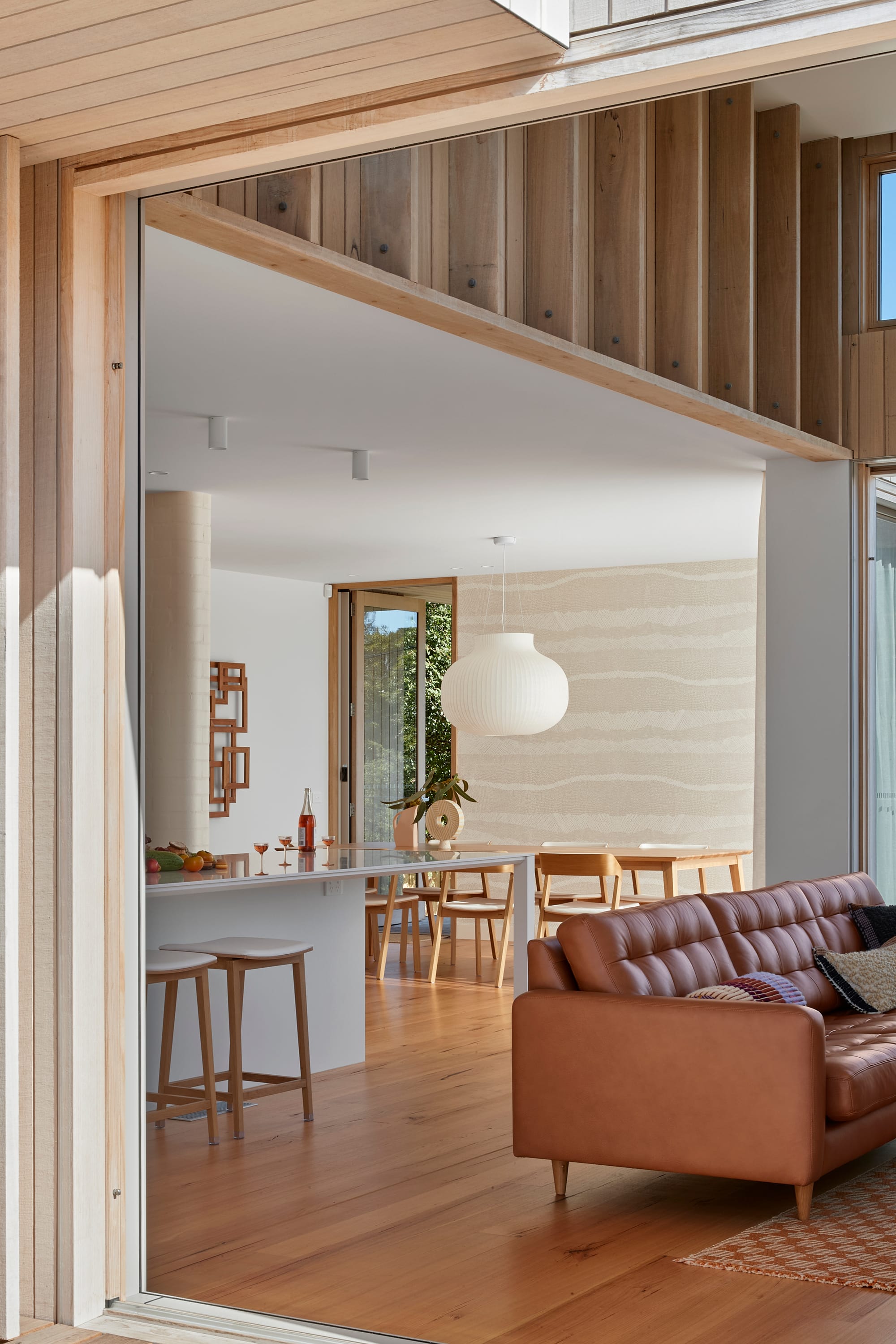 The Blairgowrie Beach Club by Bower Architecture & Interiors. Photography by Shannon McGrath. A window overlooking kitchen countertop and brown colored sofa.