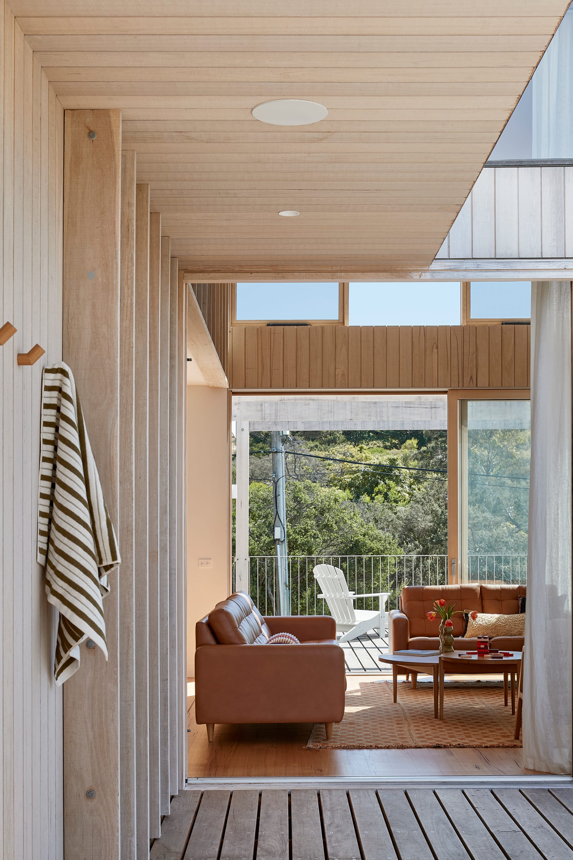 The Blairgowrie Beach Club by Bower Architecture & Interiors. Photography by Shannon McGrath. Close up view from patio into the living room with brown sofas.