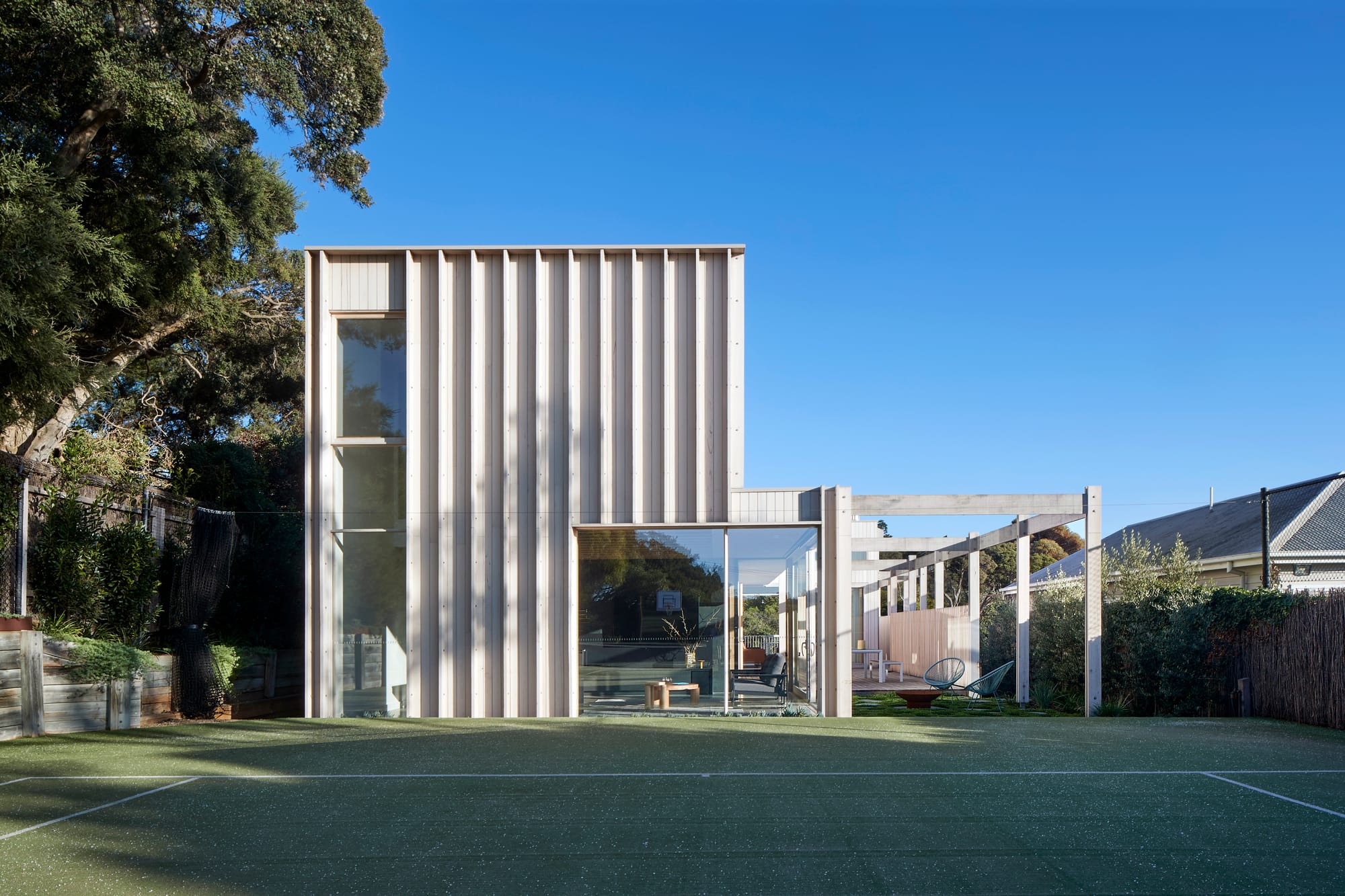 The Blairgowrie Beach Club by Bower Architecture & Interiors. Photography by Shannon McGrath. A person playing tennis infront of two storey house.