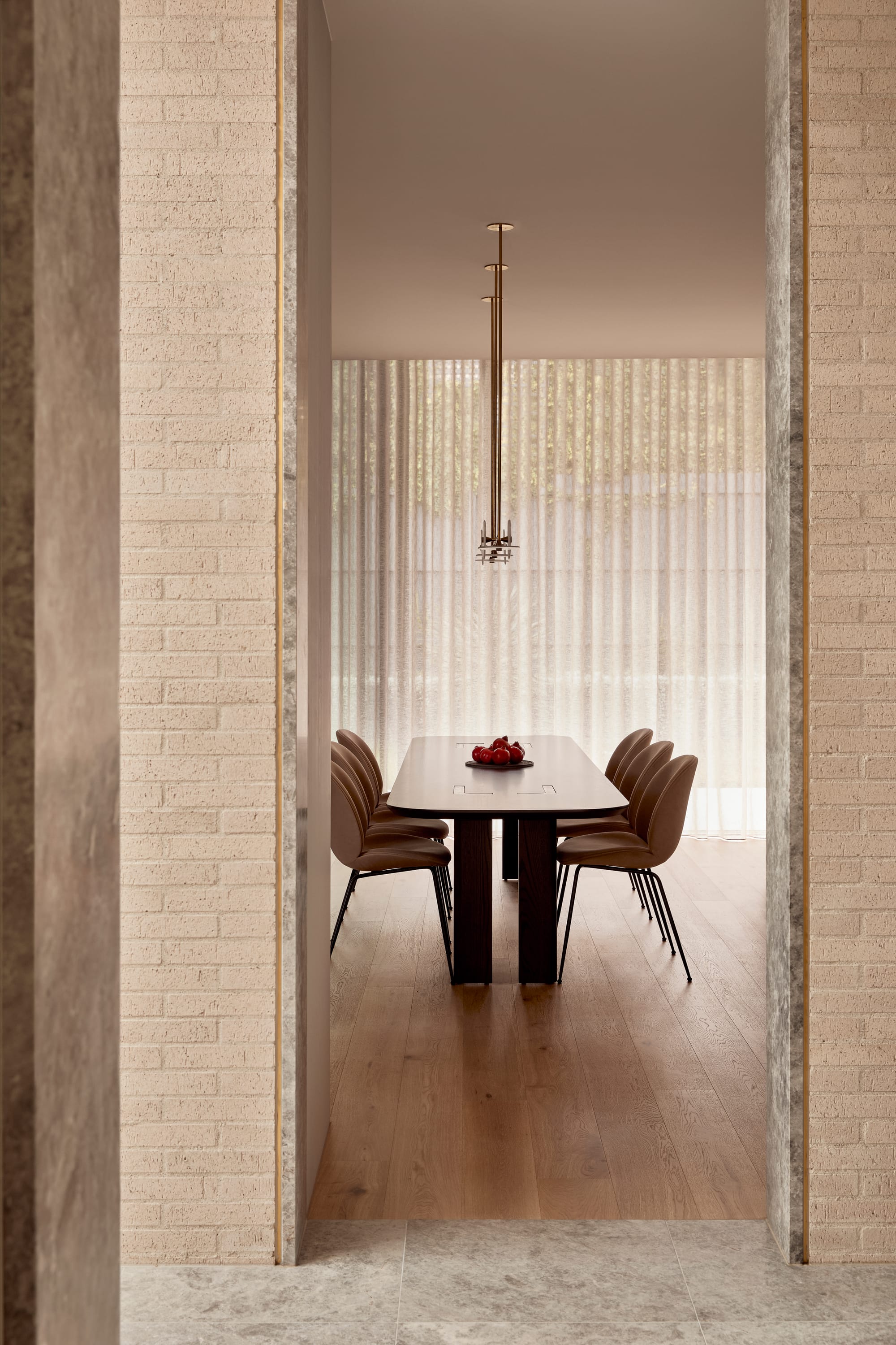 Brixton by Cera Stribley. Photography by Martina Gemmola. Framed view into an elegant dining room with a dark timber table, soft leather chairs, sheer curtains, and a sculptural brass pendant light.